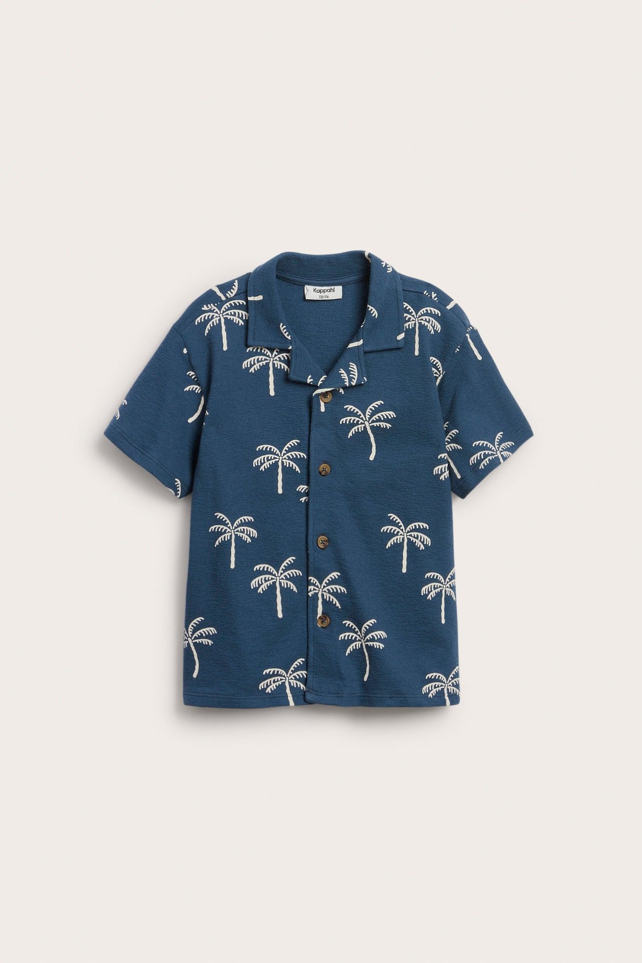 Widok z przodu niebieskiej koszuli bawełnianej dla dziecka z krótkim rękawem, białym wzorem palm i guzikami.