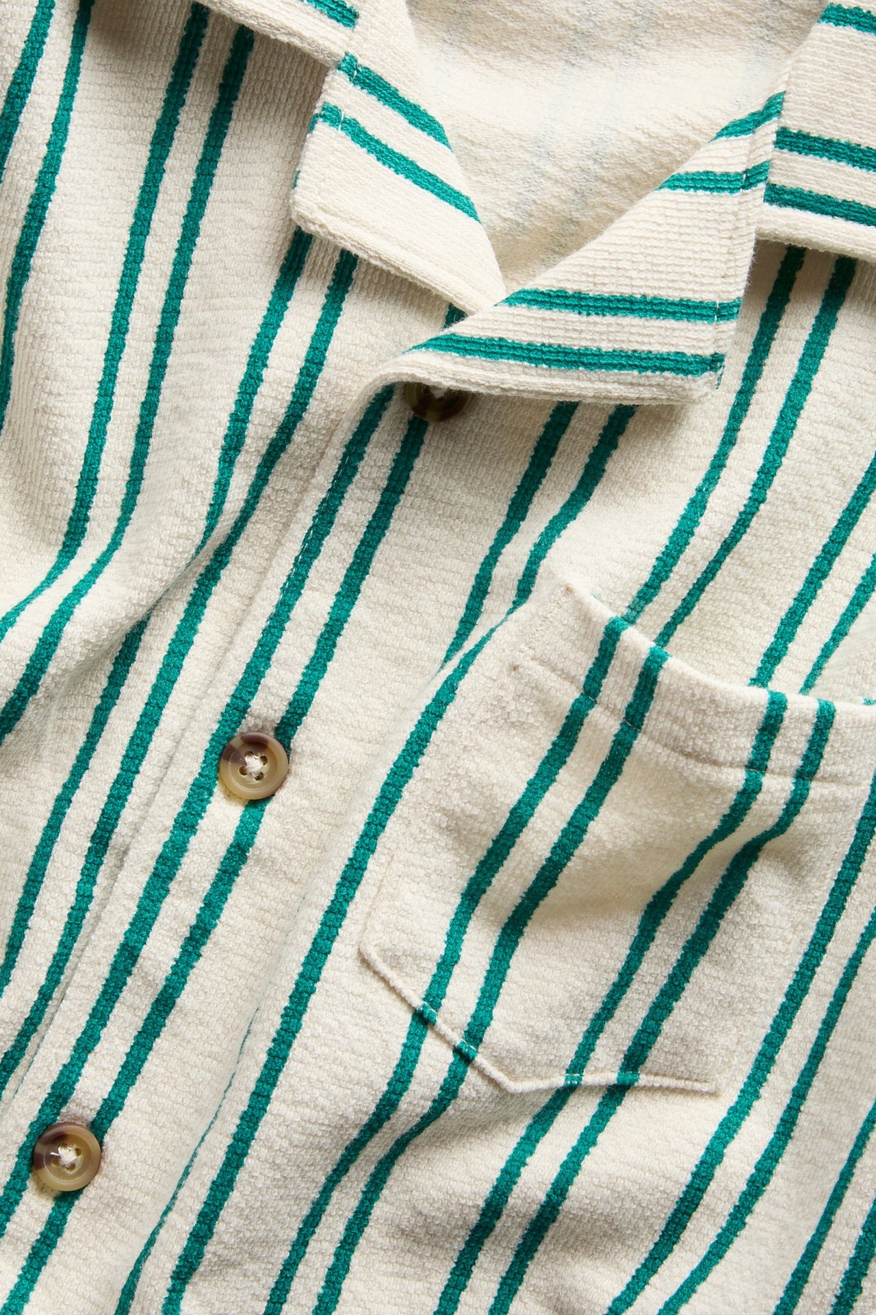 Zbliżenie z przodu: kremowa koszula z bawełnianej dzianiny w zielone paski, z brązowymi guzikami i kieszenią.