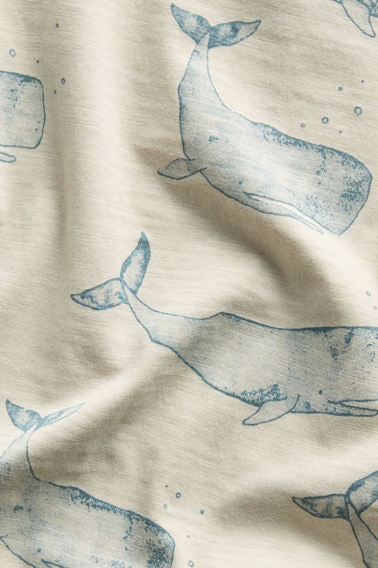Zbliżenie beżowego bawełnianego body niemowlęcego z dzianiny slub z niebieskim nadrukiem wielorybów i bąbelków.