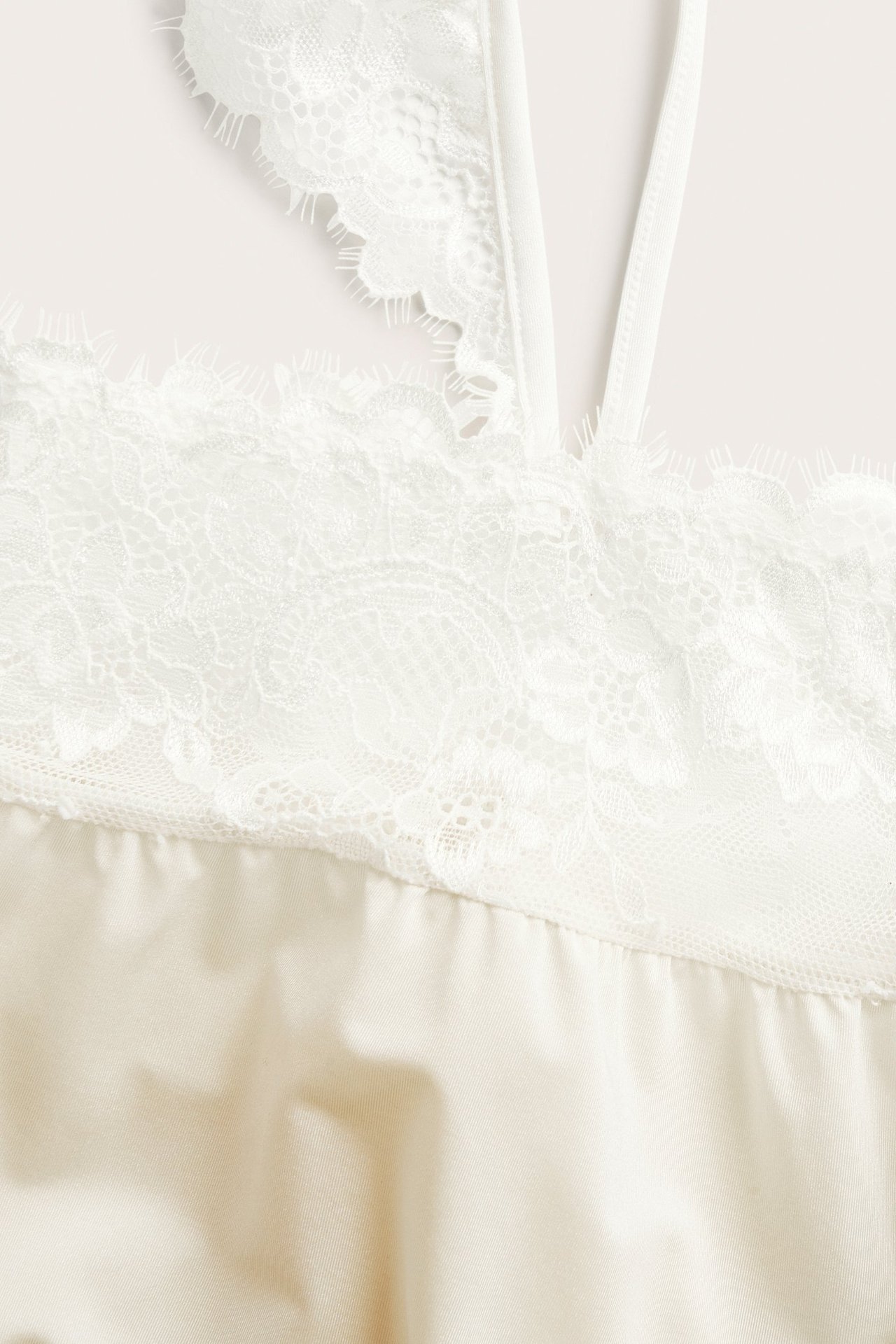 Närbild av ett offwhite satinlinne med fina spetsdetaljer och tunna axelband.
