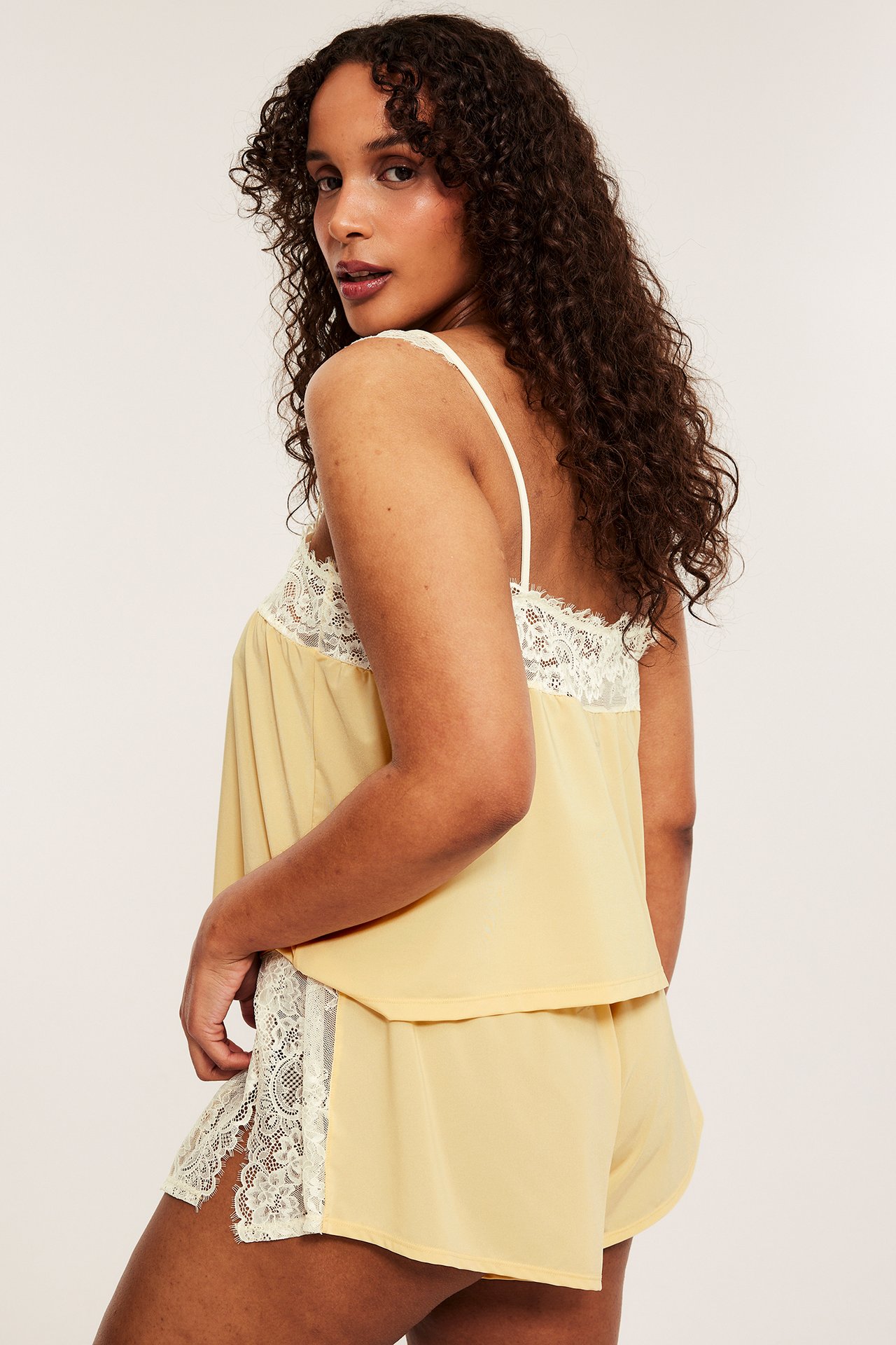 Kvinnas 3/4 bakifrån: ljusgul satinlinne med vit spets, matchas med shorts med spetsdetaljer.
