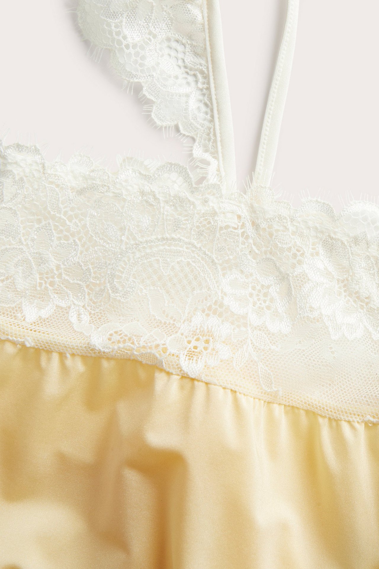 Zbliżenie jasnożółtego satynowego topu z białymi koronkowymi detalami i cienkimi ramiączkami.