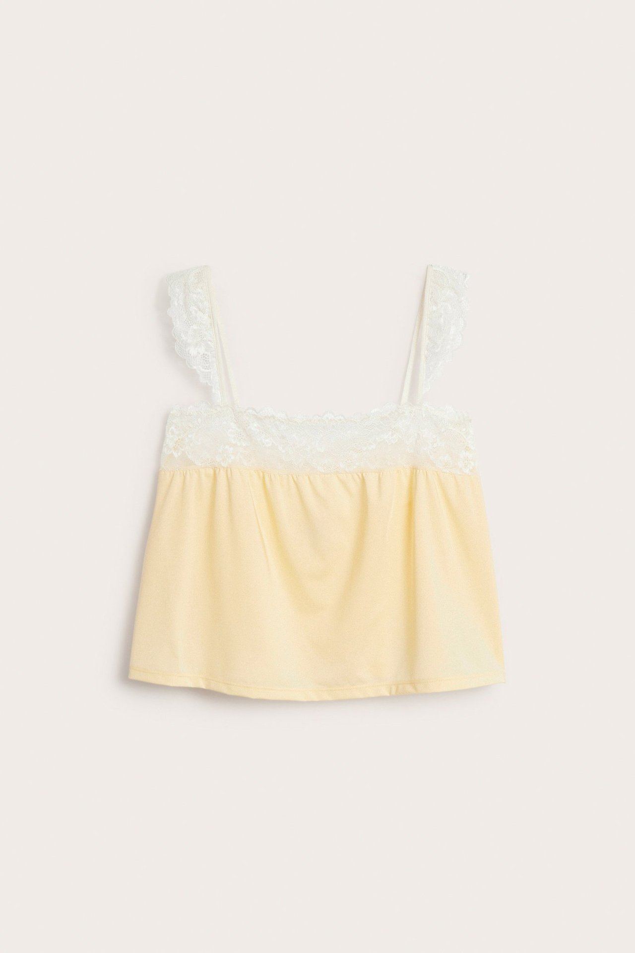 Framifrån: Ljusgul satinlinne med vit spets i halsringning och axelband.