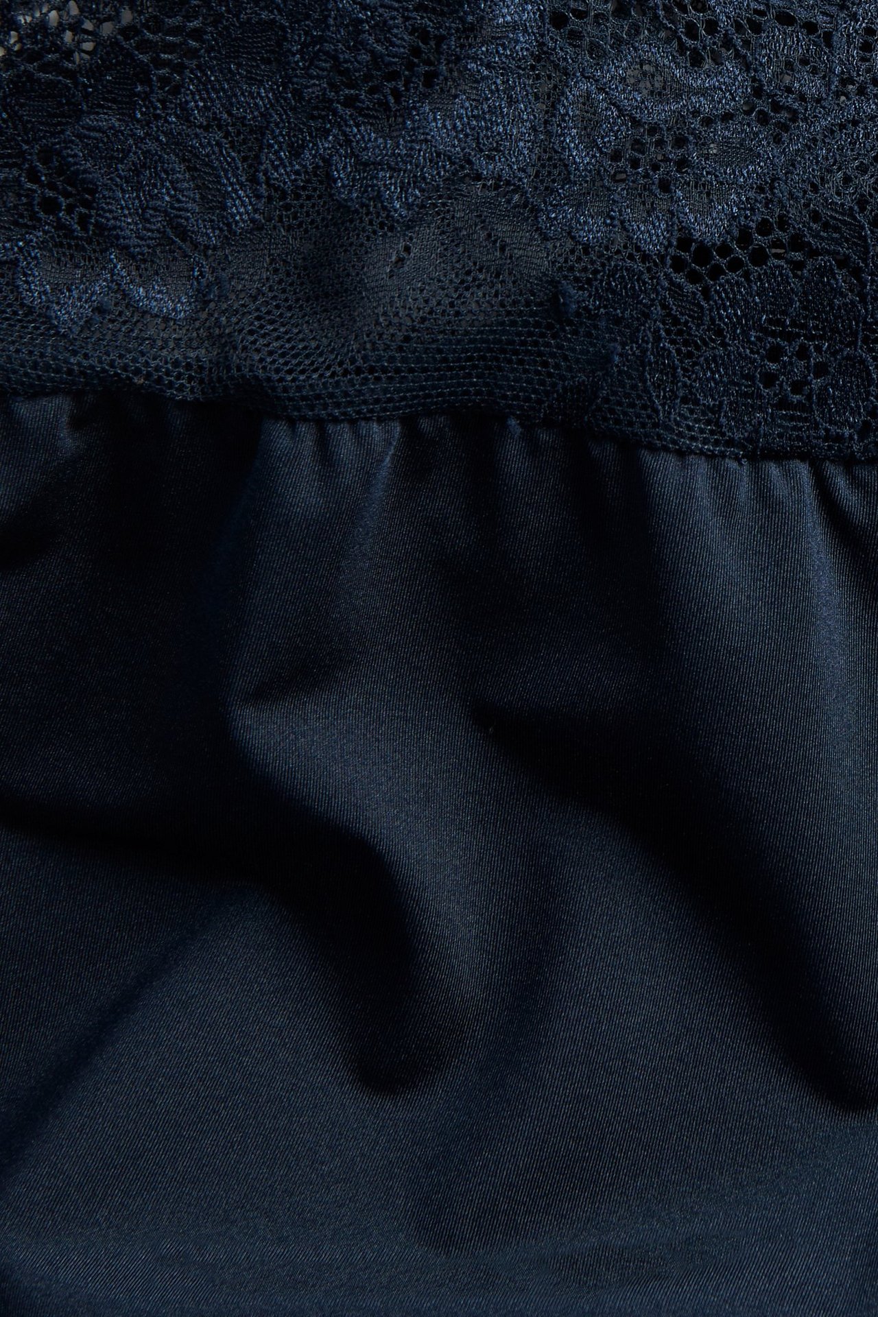 Zbliżenie na ciemnoniebieską satynową koszulkę z koronkowymi detalami.