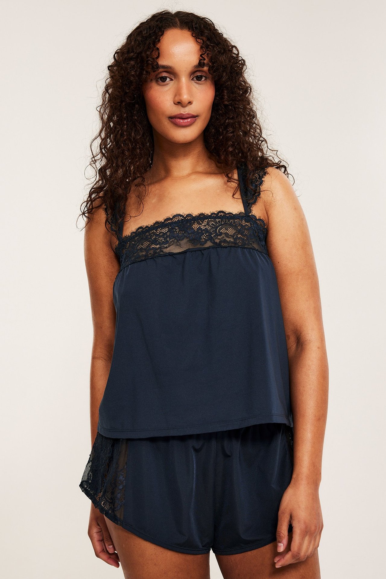 Widok z przodu kobiety w granatowej satynowej koszulce na ramiączkach z koronką i pasujących szortach.