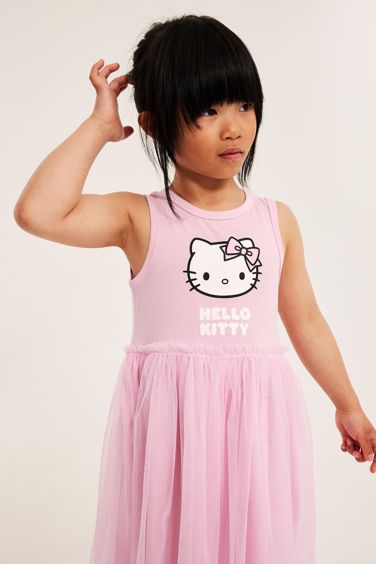 Edestäpäin lapsi vaaleanpunaisessa, hihattomassa Hello Kitty -jersey mekossa laskostetulla tyllihameella.