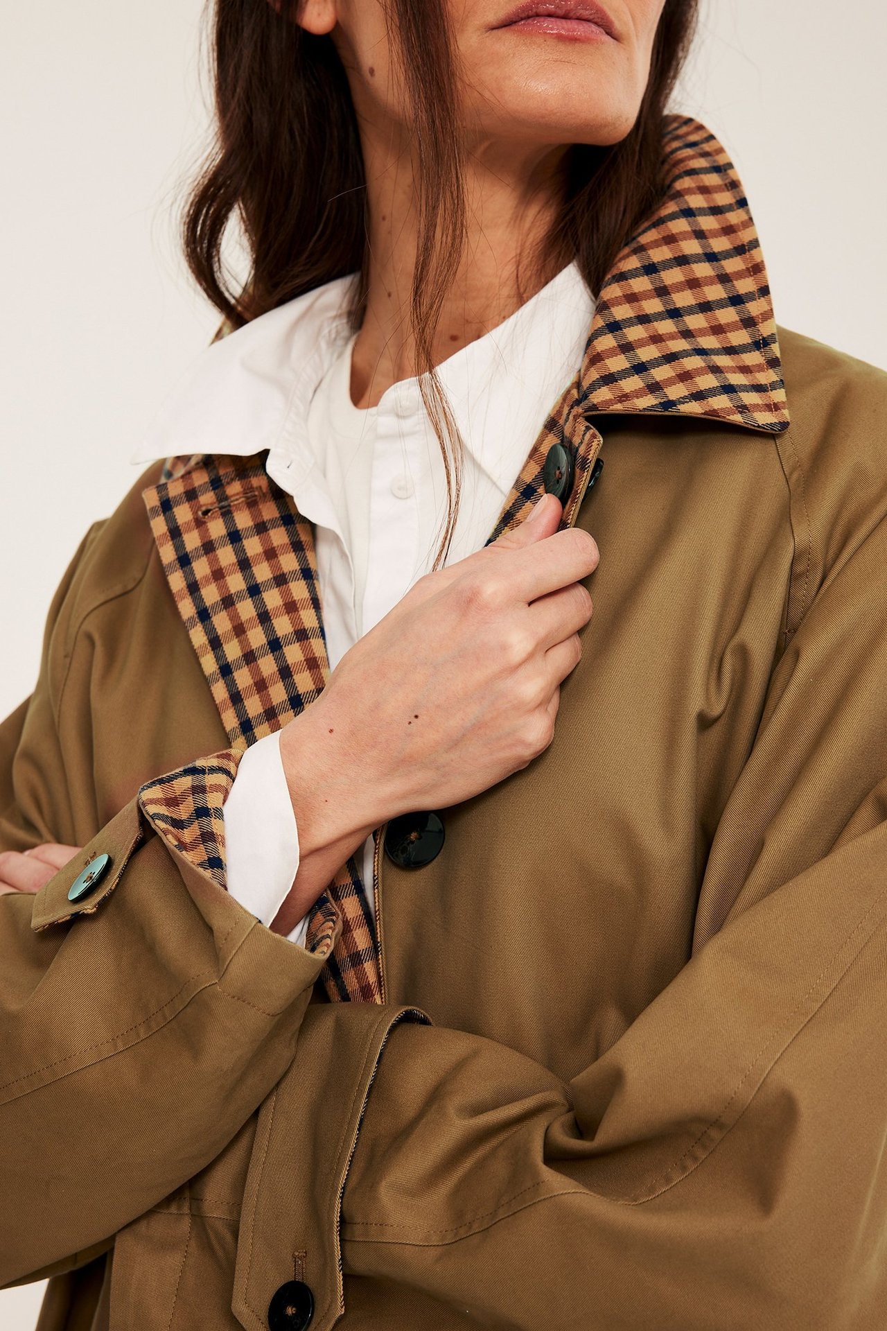 Zbliżenie na beżowy dwustronny trencz damski z brązową kratą w środku, noszony na białej koszuli.