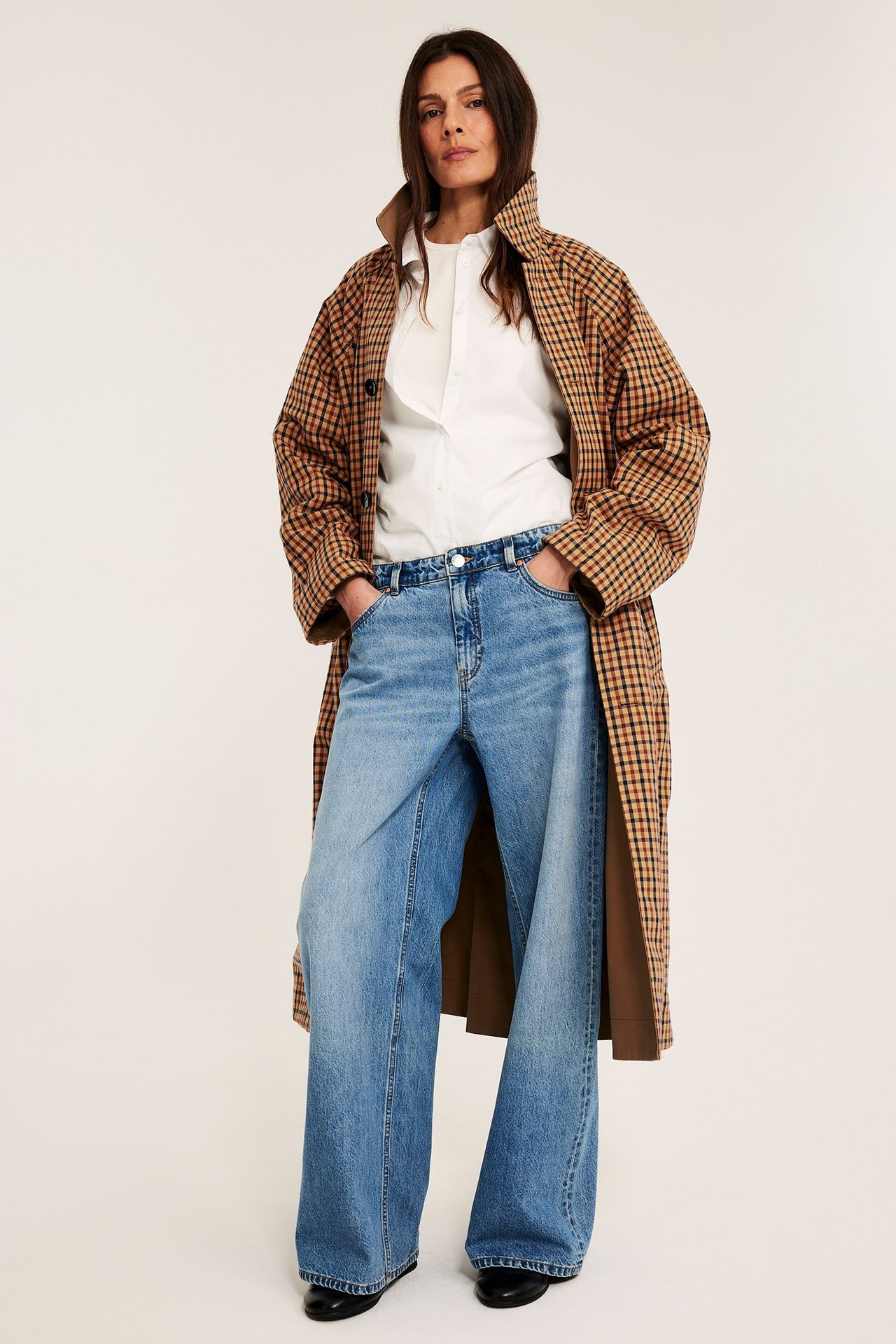 Frontbilde: Kvinne i brunrutet vendbar kåpe, hvit skjorte, lyseblå jeans og svarte sko.