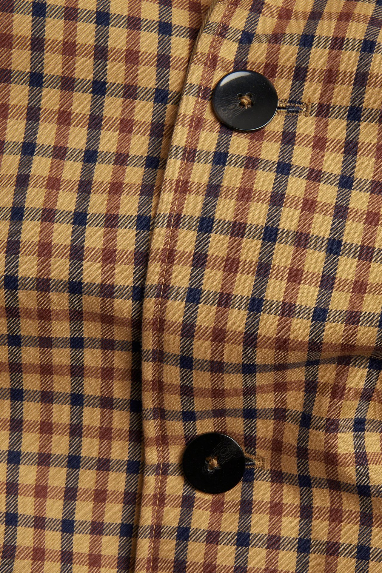 Nærbilde av en beige, brun og mørkeblå rutet vendbar kåpe med to svarte knapper.