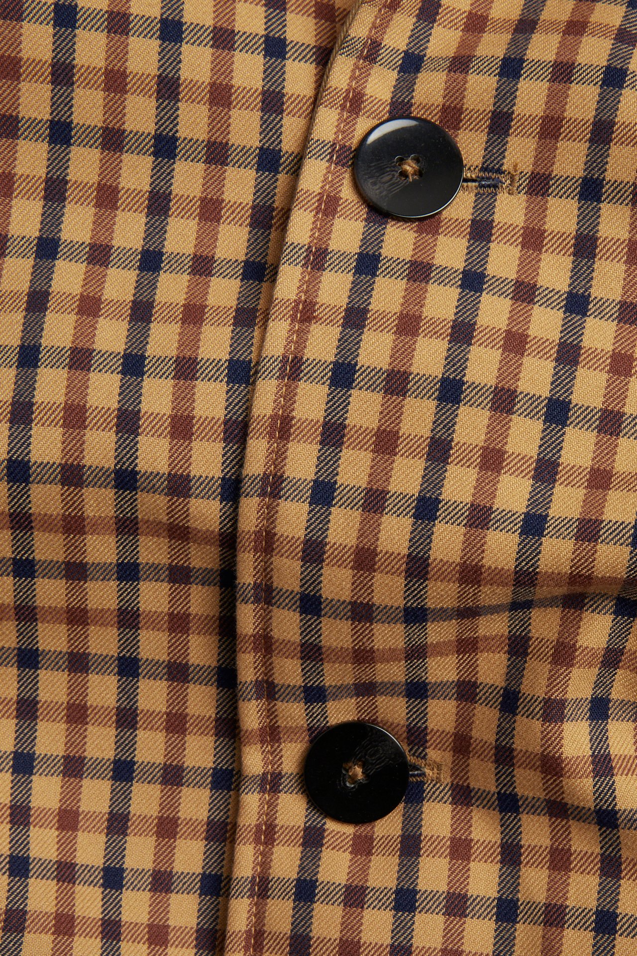 Nærbilde av en vendbar trenchcoat i beige, brun og blå rutete med to svarte knapper.