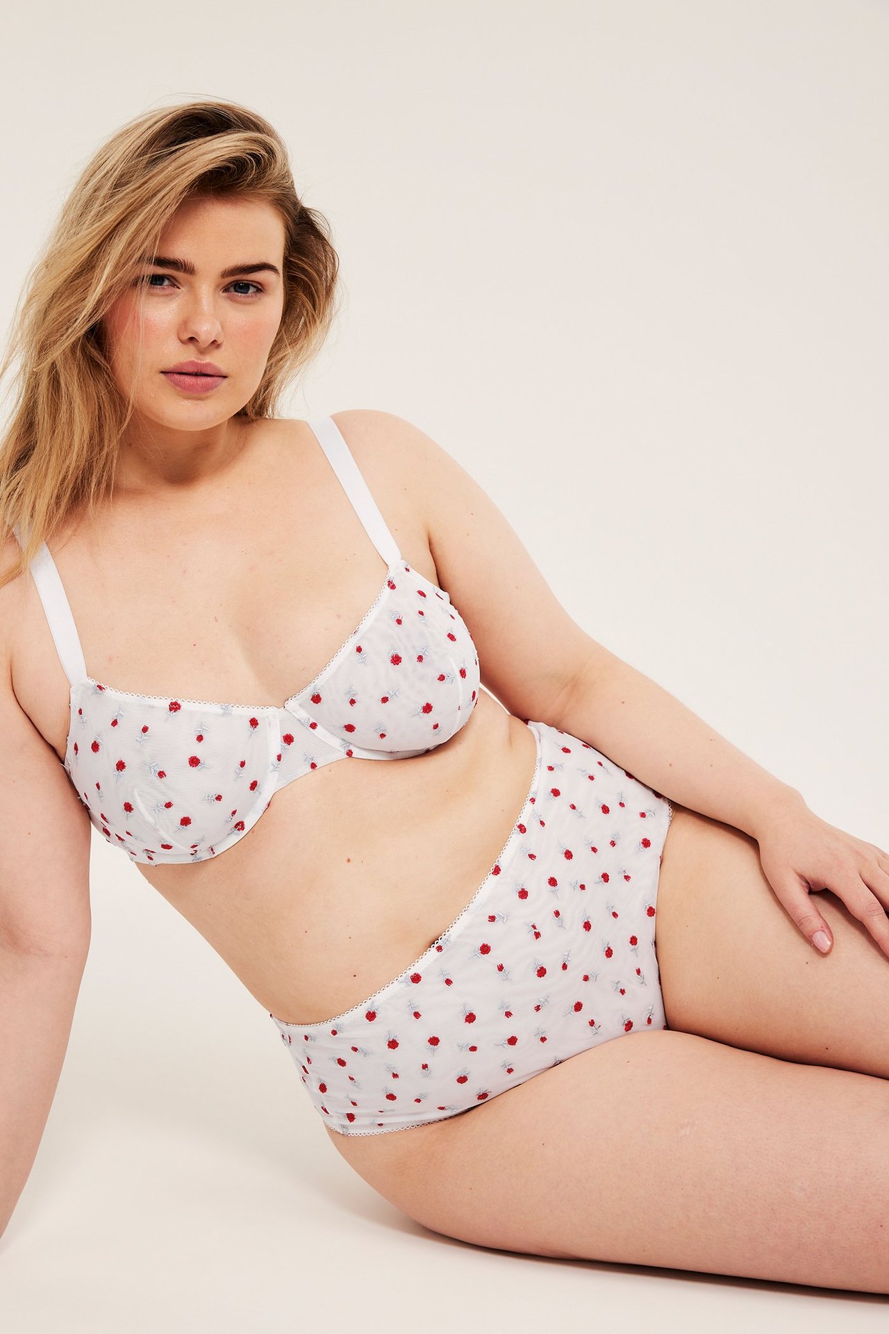 Forfra, kvinne i offwhite netting-BH med spiler og matchende truse med broderte røde roser.