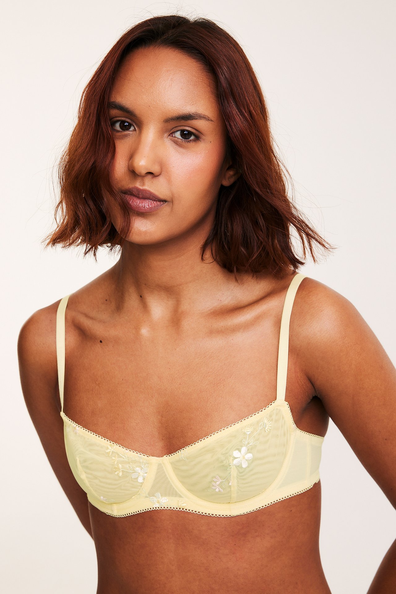 Framifrån, kvinna i ljusgul bygel-bh i mesh med vit blombrodyr.