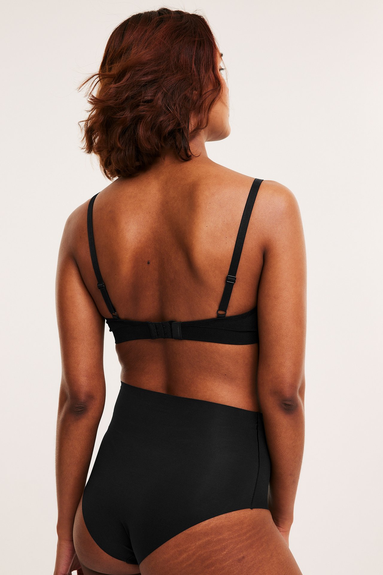 Widok z tyłu kobiety w czarnych bezszwowych majtkach modelujących z wysokim stanem i pasującym czarnym biustonoszu.