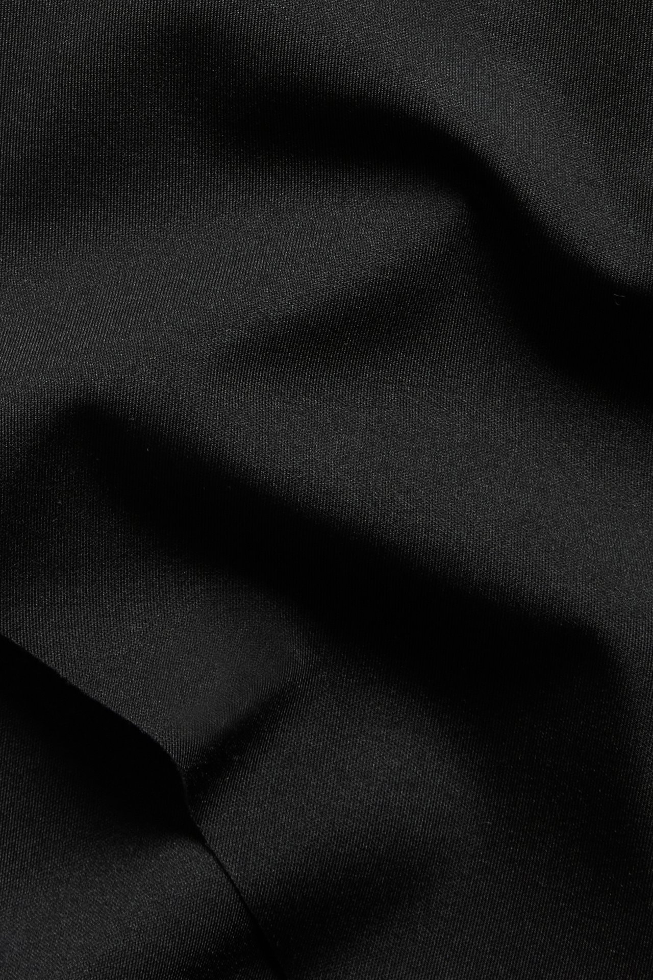 Lähikuva mustasta kevyesti muokkaavasta brief-housusta, joka näyttää sileän, yksivärisen polyamidi-elastaanikankaan hienoisilla rypyillä.