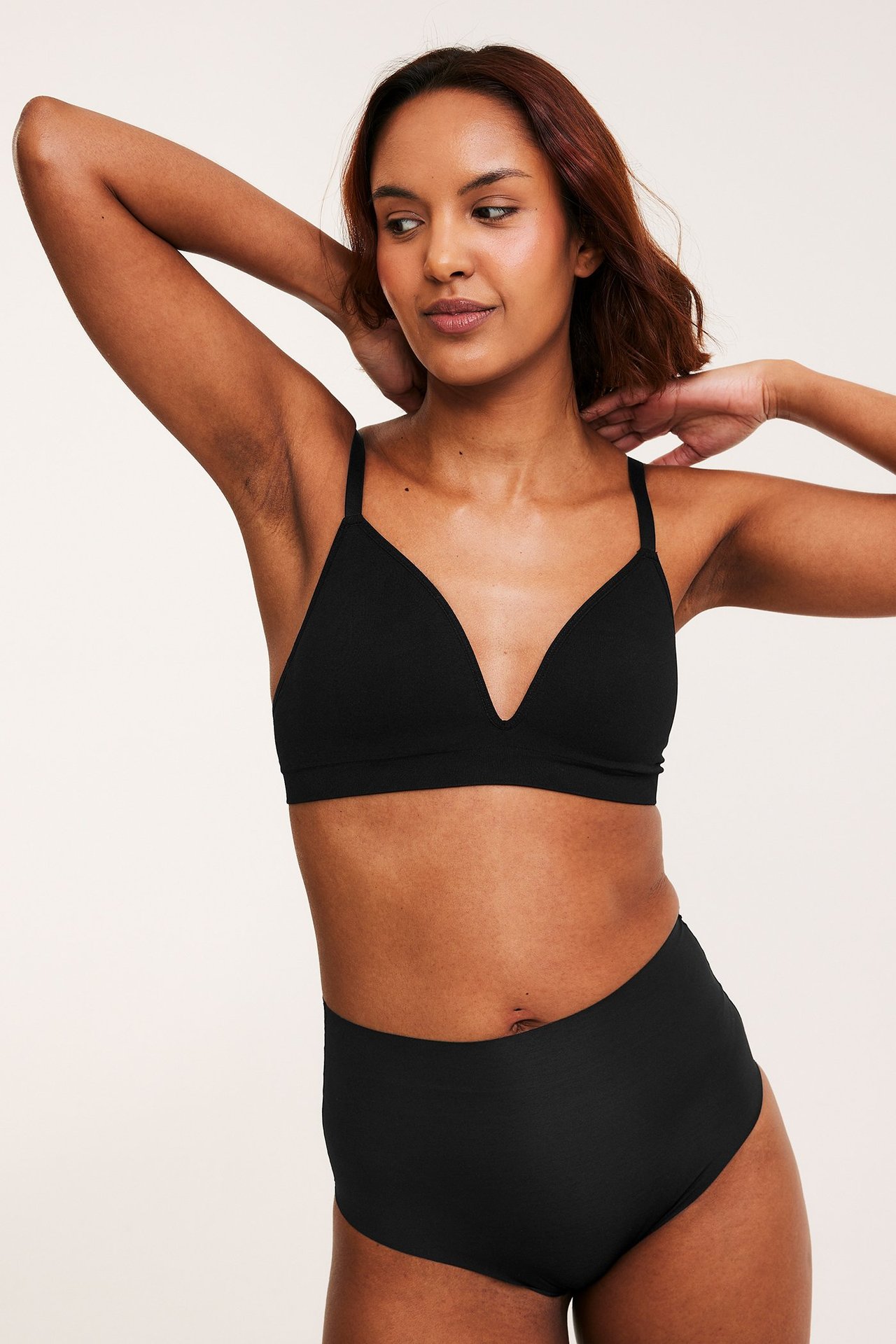 Framsida: Kvinna i svarta sömlösa high-waist trosa och matchande svart sömlös bralette.