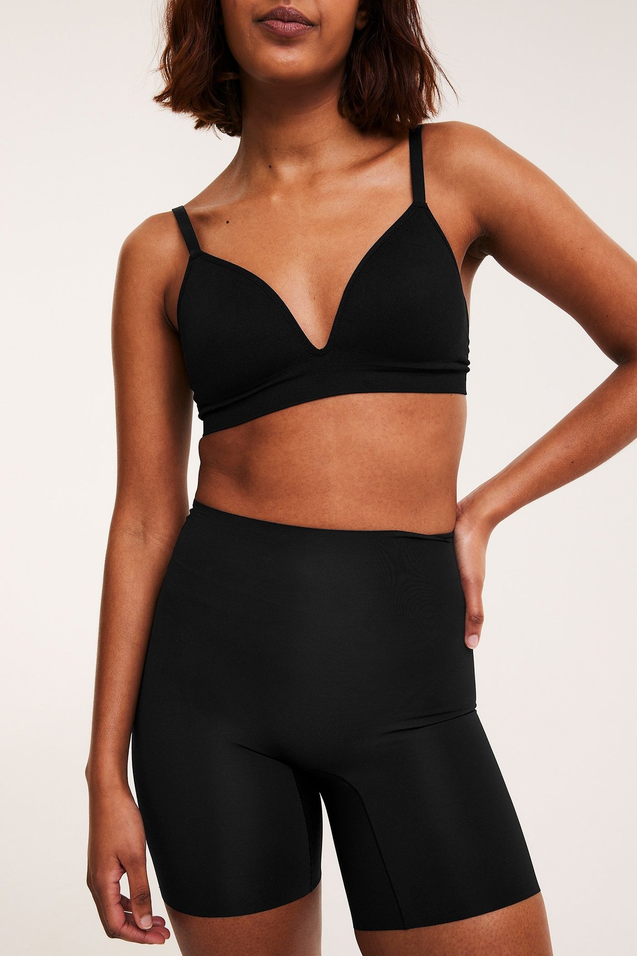 Forfra, kvinne iført svarte sømløse shapingshorts med høyt liv og en matchende svart myk BH.