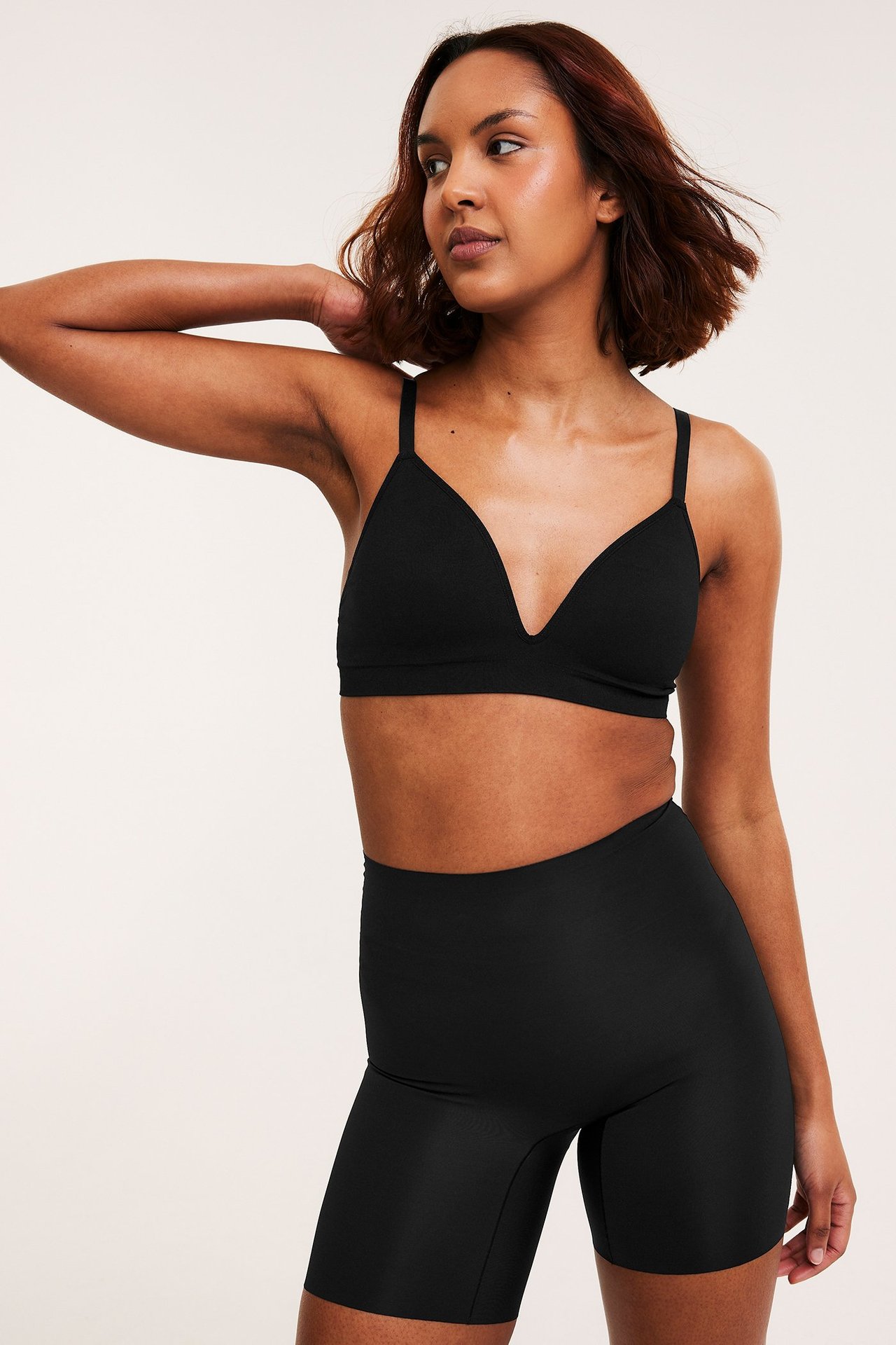 Framifrån en kvinna i svarta sömlösa höga shapingshorts med lätt formning och matchande svart sömlös behå.