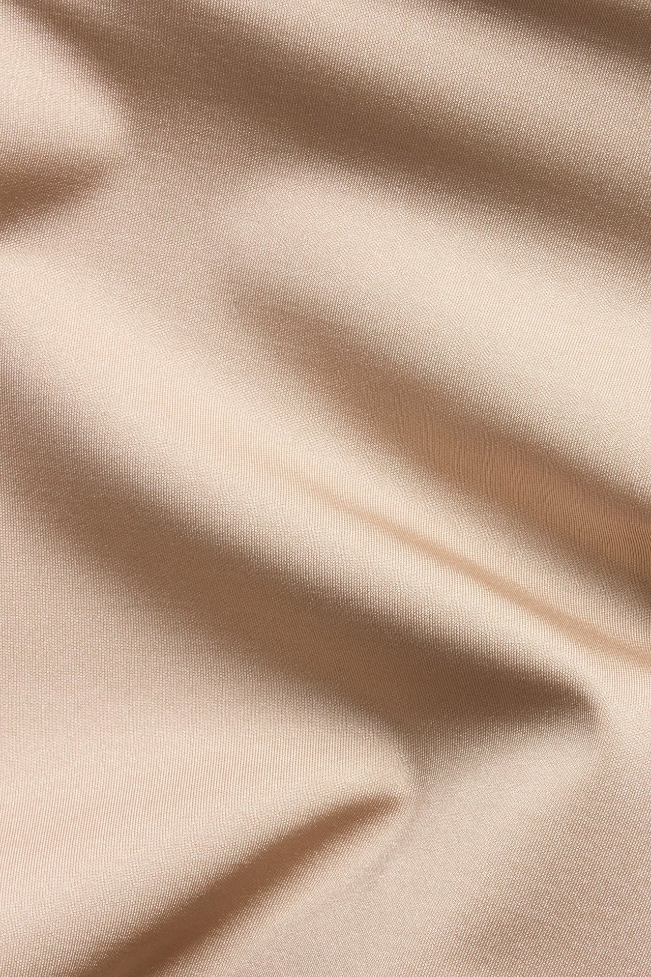 Lähikuva vaaleanruskeasta saumattomasta muotoilukankaasta, jossa hienovaraisia laskoksia ja hieno rakenne.
