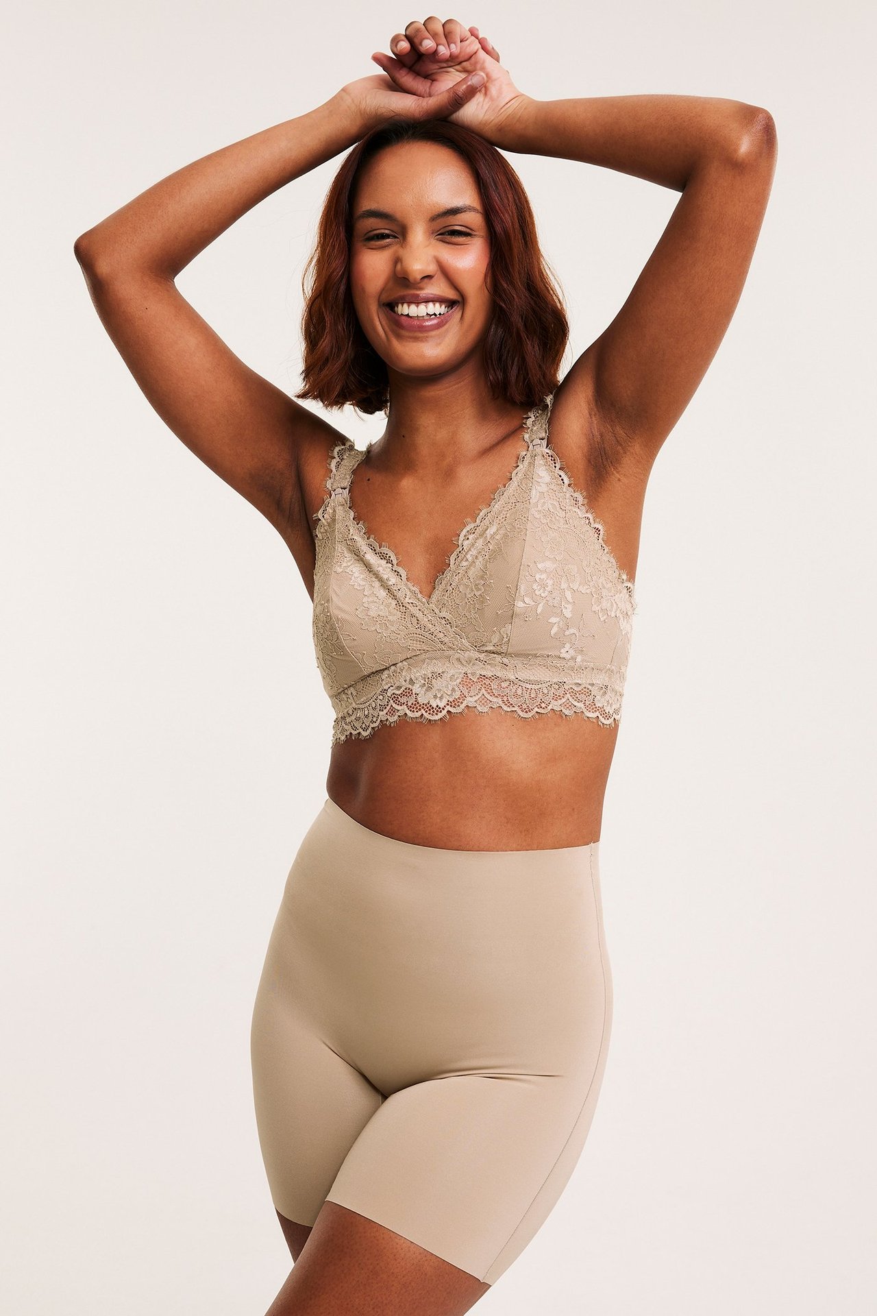 Forfra, smilende kvinne i lys brune shapingshorts med høy midje og matchende blonde-bh.