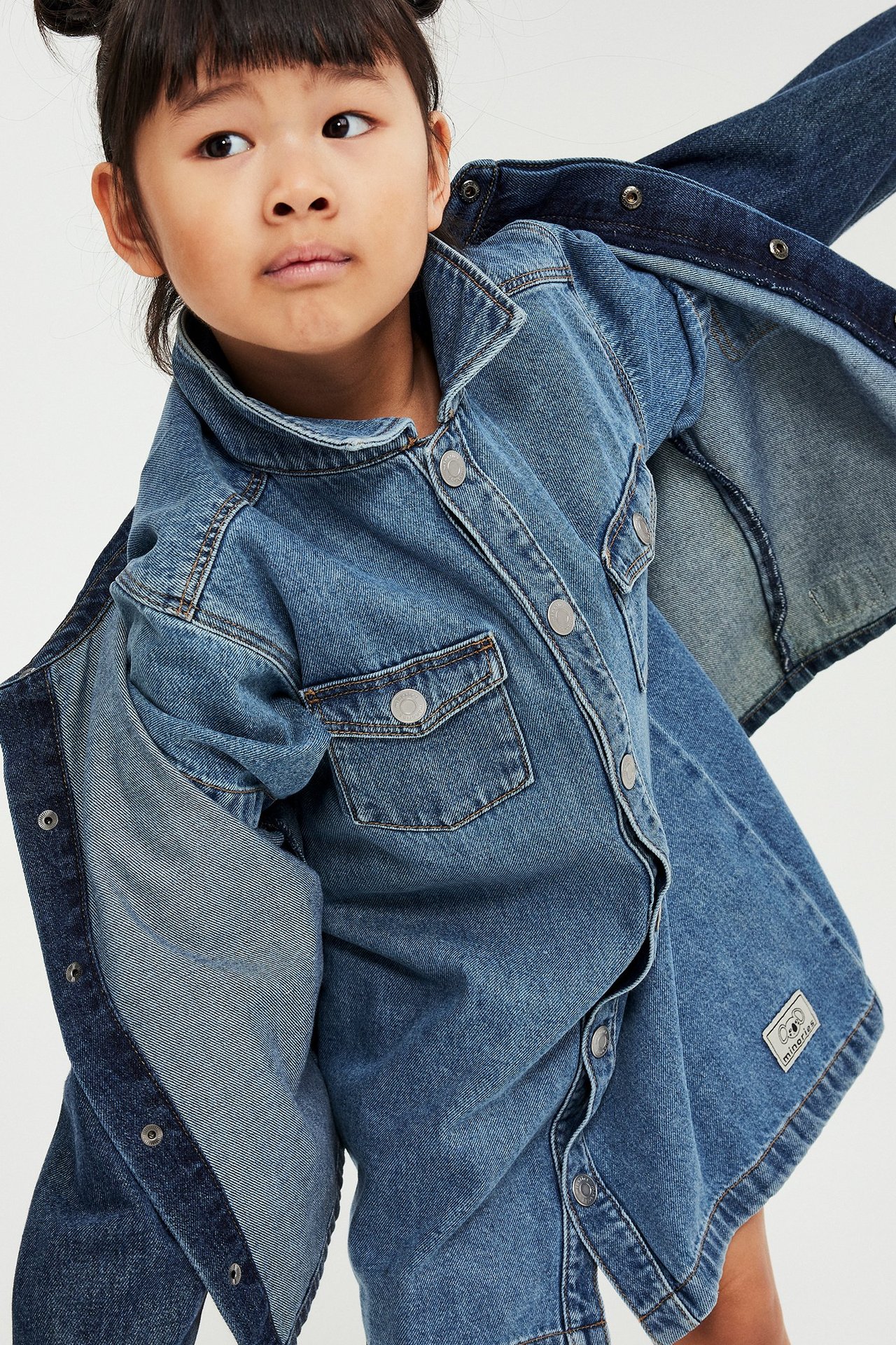 Etunäkymä lapsesta, jolla on sininen lyhythihainen denim-mekko, jossa on kaulus, etutaskut ja nepparit.