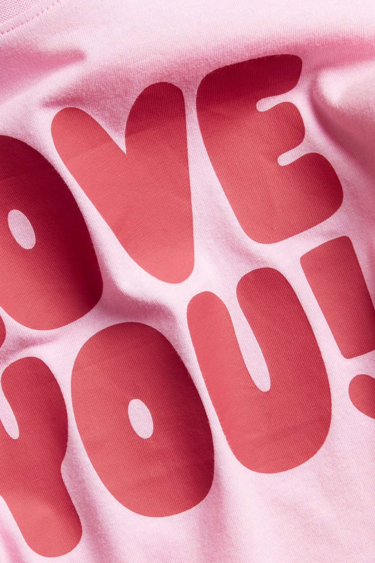 Zbliżenie na jasnoróżowy bawełniany T-shirt z czerwono-różowym nadrukiem tekstowym "LOVE YOU!" z przodu.