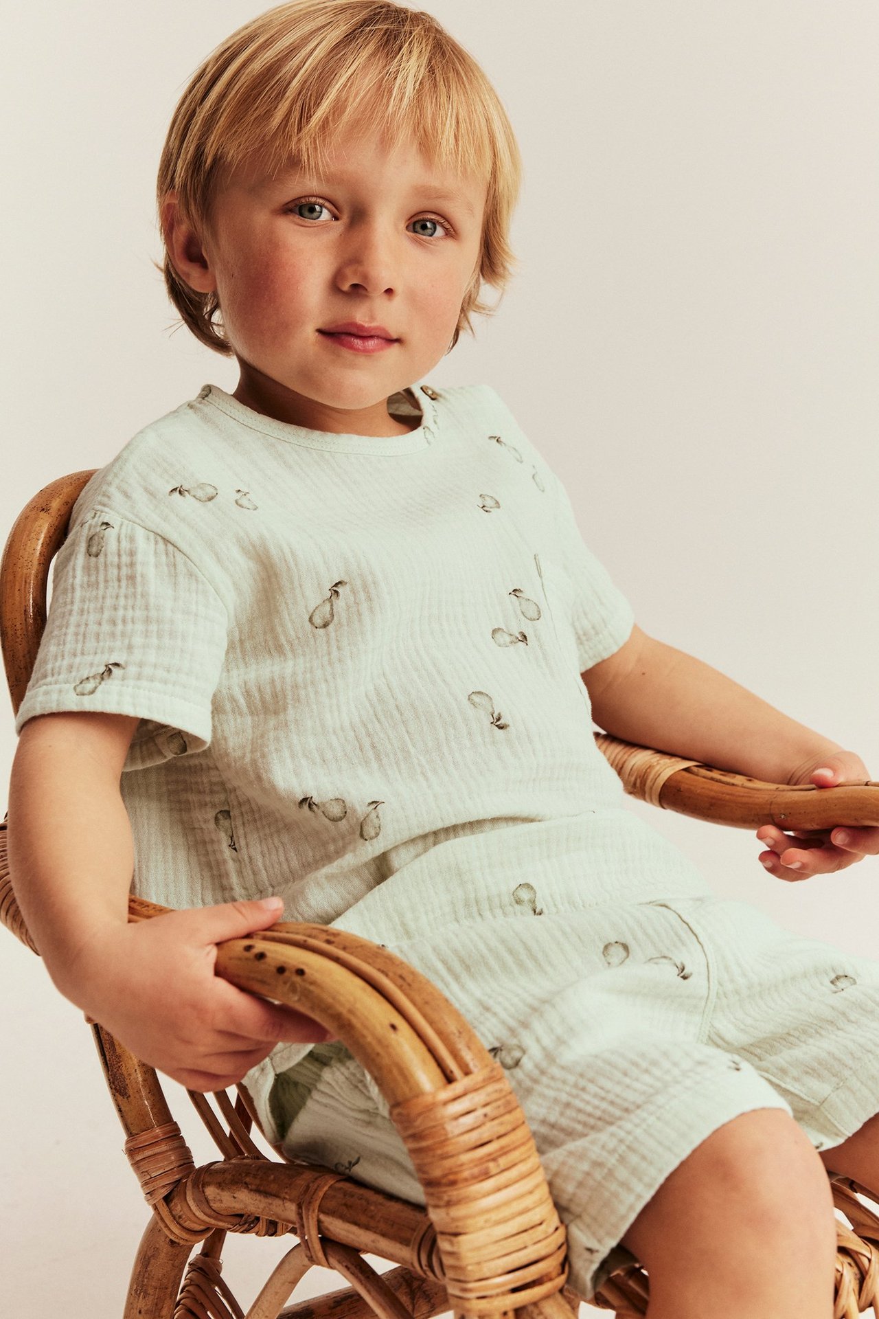Edestäpäin, lapsi yllään vaaleanvihreä päärynäkuvioitu lyhythihainen puuvillamusliinitoimi ja yhteensopivat shortsit.