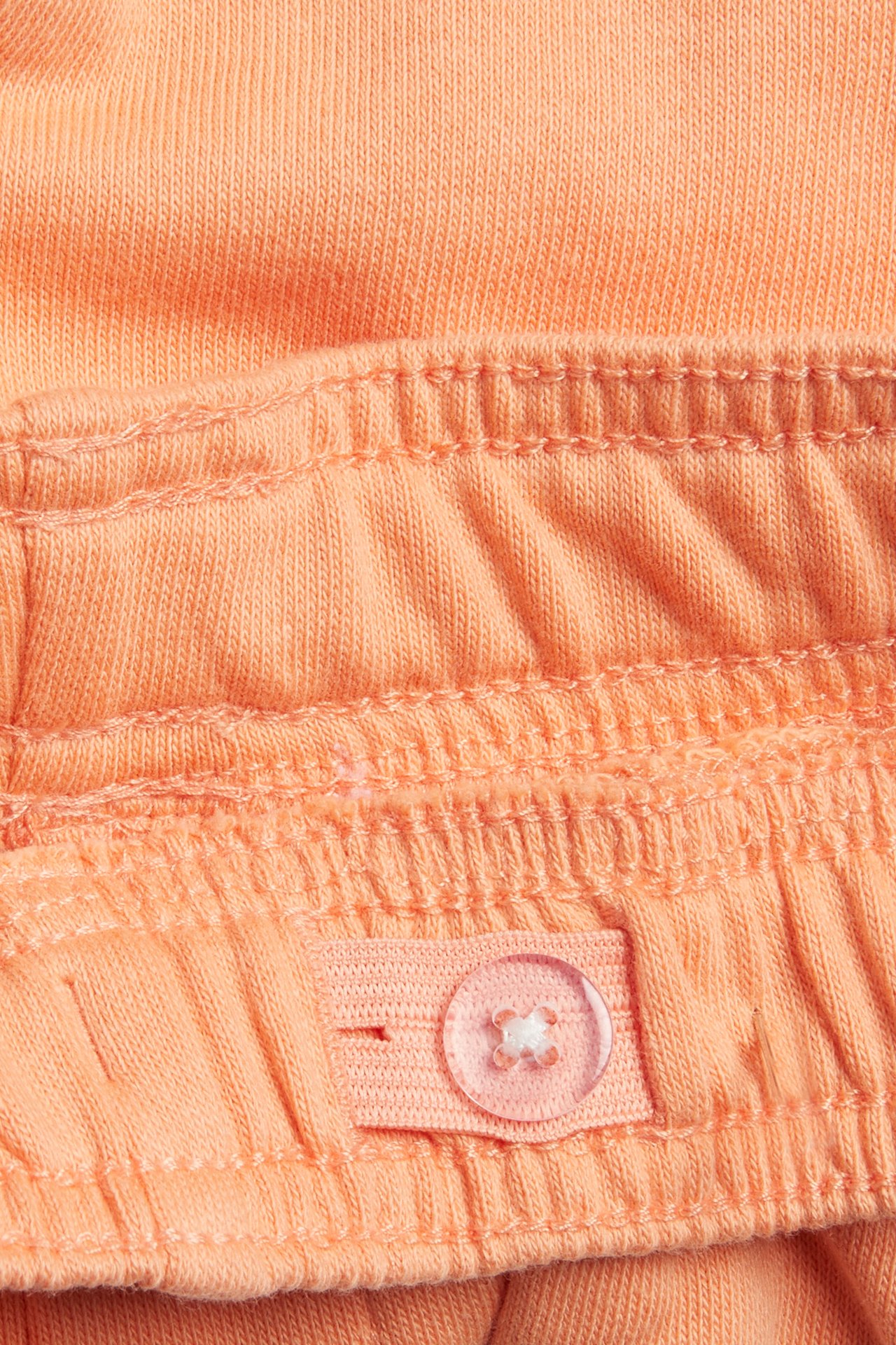 Lähikuva oransseista jersey-shortseista, joissa joustava vyötärö ja säädettävä läpinäkyvä nappi.