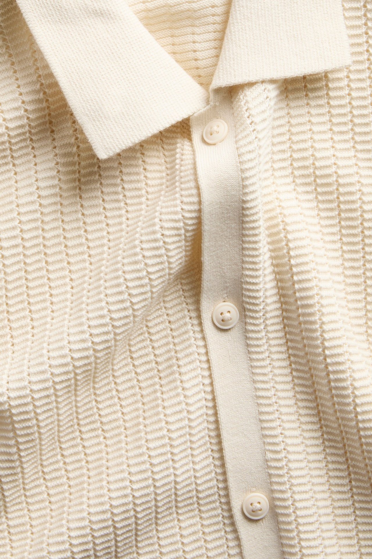Widok z przodu: Beżowa koszulka polo z krótkim rękawem, teksturowanym splotem i białymi guzikami.