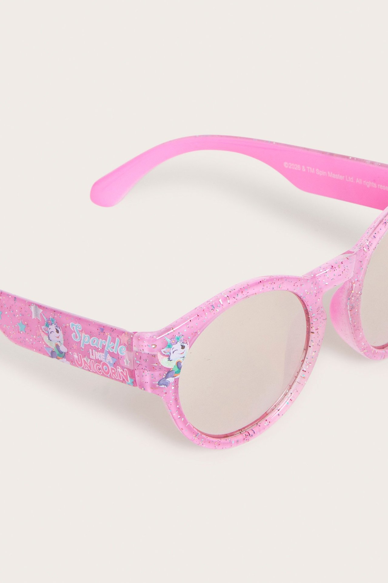 Zbliżenie na różowe brokatowe plastikowe okulary przeciwsłoneczne z napisem "Sparkle Like a Unicorn" i grafikami jednorożców.