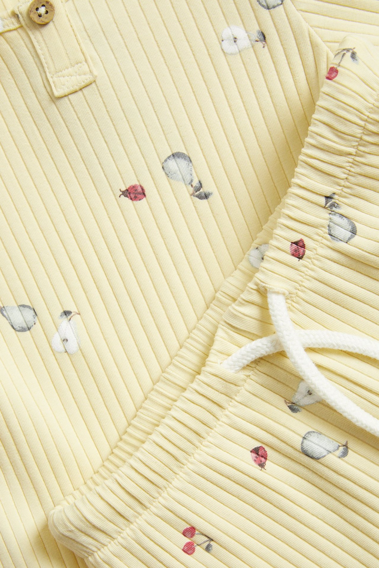 Zbliżenie żółtego, prążkowanego zestawu 2-częściowego z wzorem gruszek, wiśni i biedronek, z guzikami i białym sznurkiem.