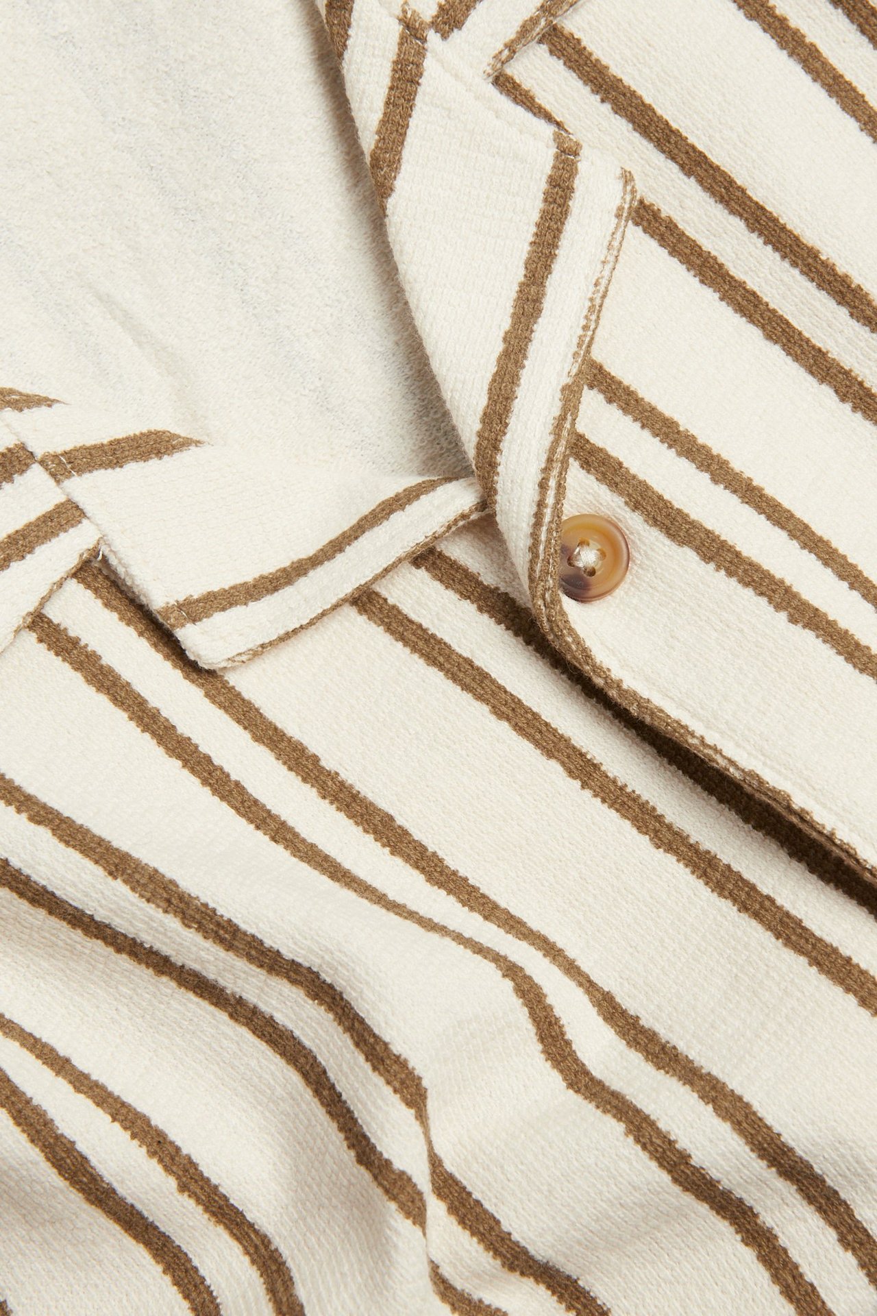 Zbliżenie kremowo-brązowej koszulki bawełnianej w paski z kołnierzem resortowym i brązowym guzikiem.