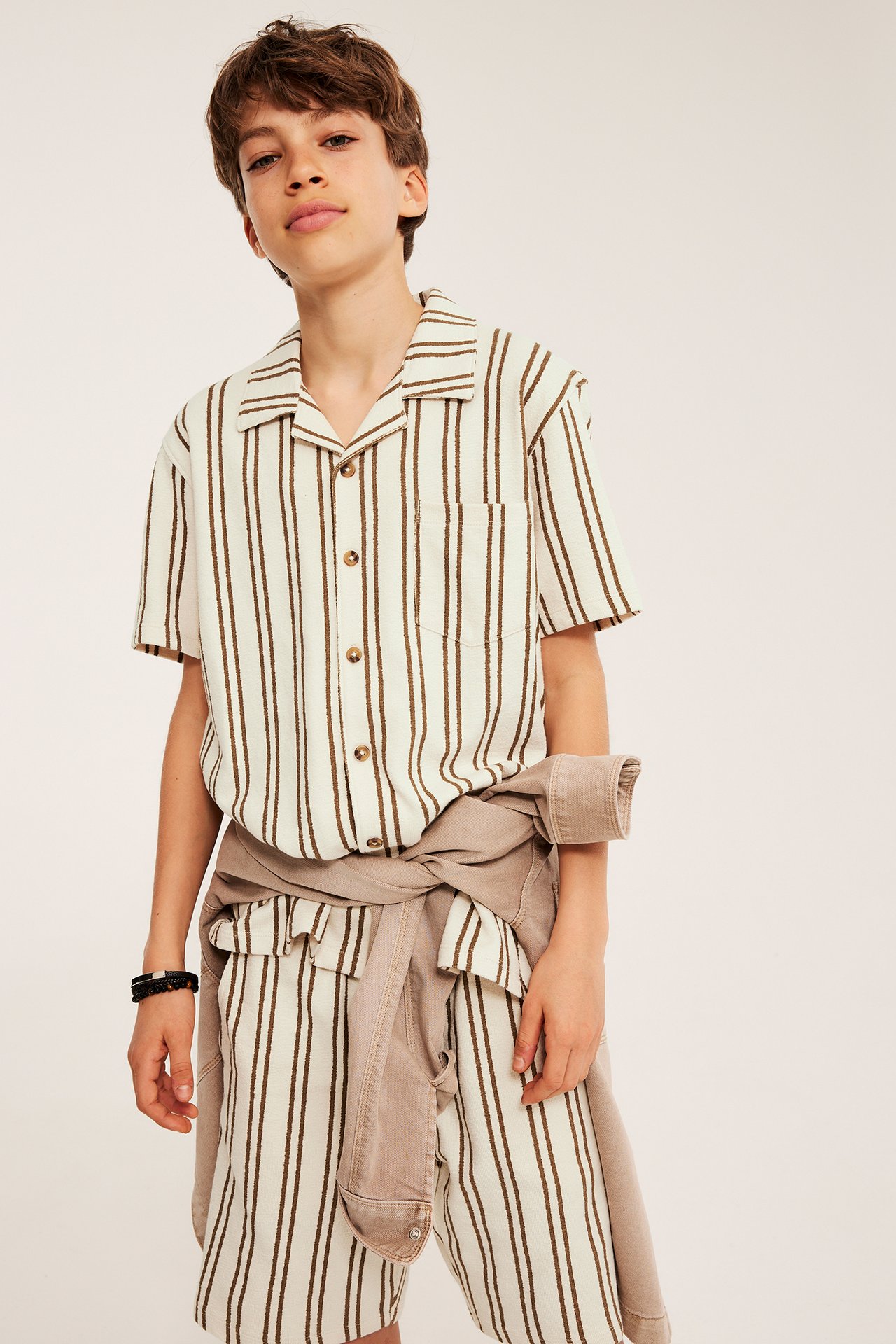 Edestä: Lapsi yllään valko-ruskea raidallinen neulepaita, yhteensopivat shortsit ja vaaleanruskea takki vyötäröllä.