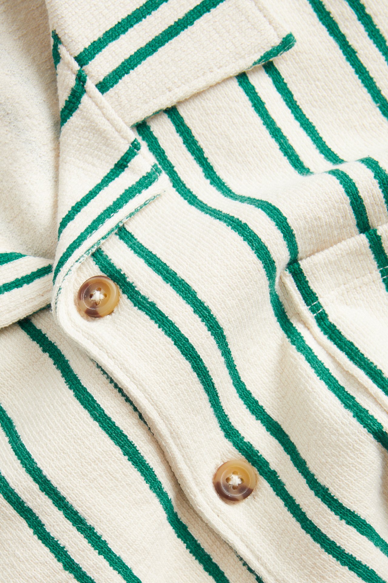 Lähikuva kermanvärisestä ja vihreäraidallisesta kuvioidusta puuvillapaidasta ruskeilla napeilla.