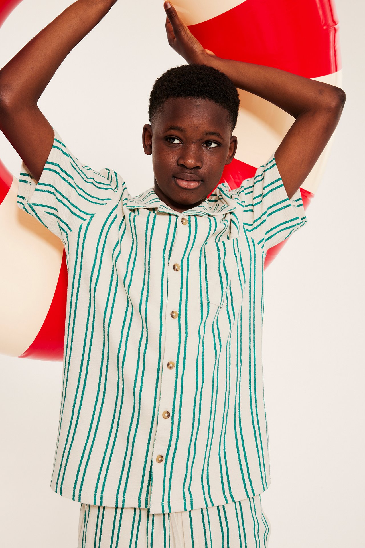 Lapsi yllään vihreä-luonnonvalkoraidallinen lyhythihainen paita, vastaavat shortsit, pitäen rengasta.