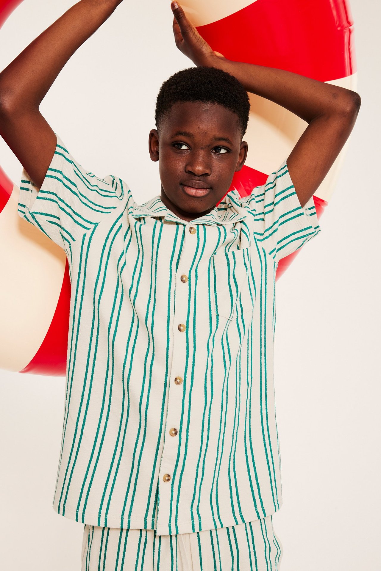 Barn bär en grön och benvit randig kortärmad skjorta, matchande shorts, och håller en ring.