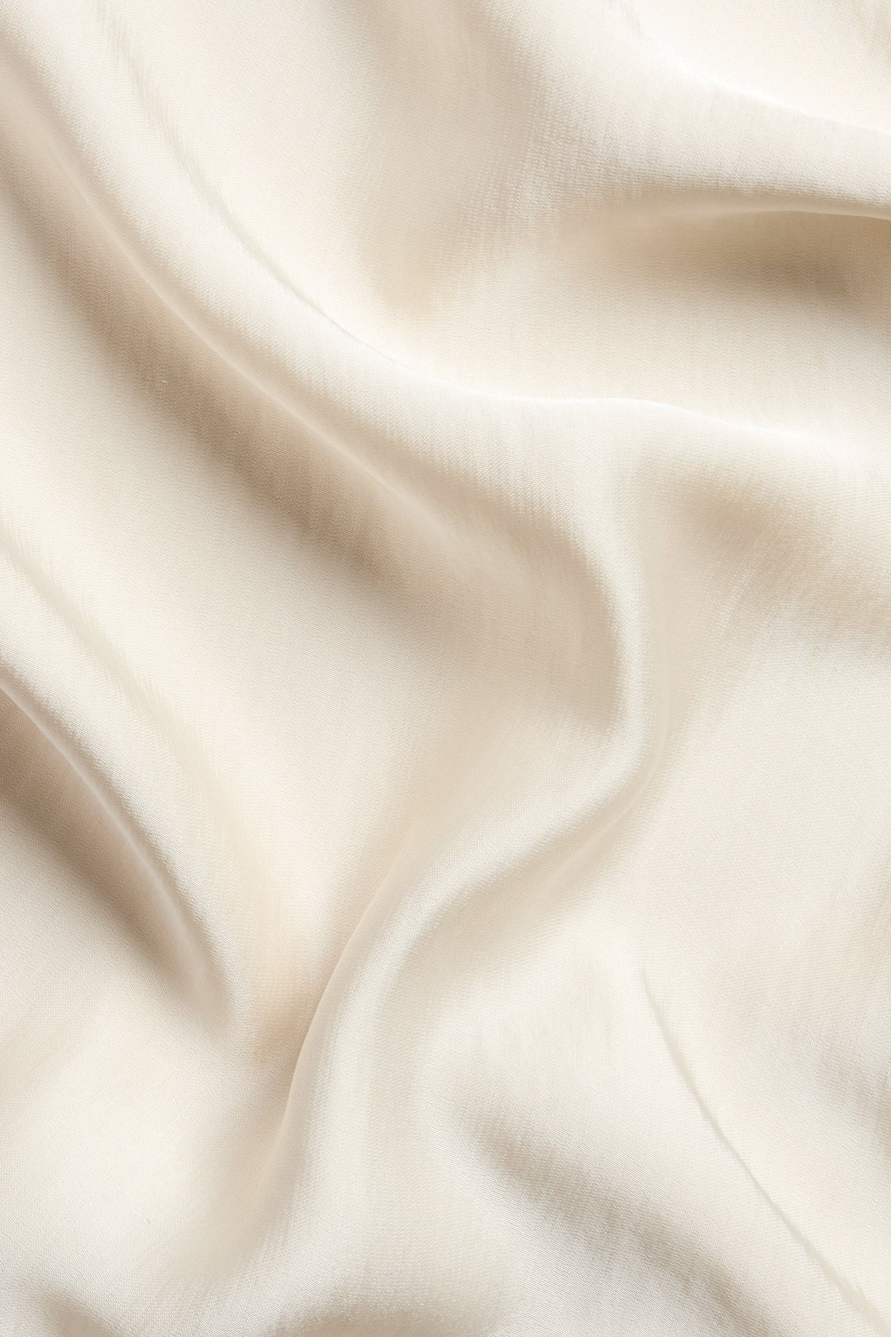 Zbliżenie na kremowy, jednolity, lejący się materiał z satyny poliestrowej na spódnicę.