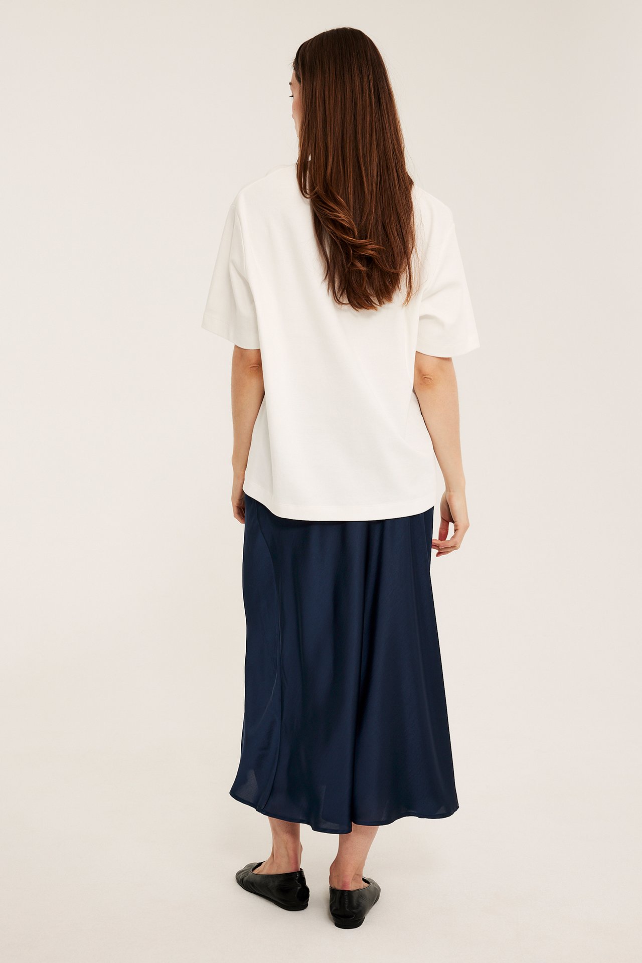 Baksida av kvinna i mörkblå utsvängd satinkjol, vit kortärmad topp och svarta ballerinaskor.