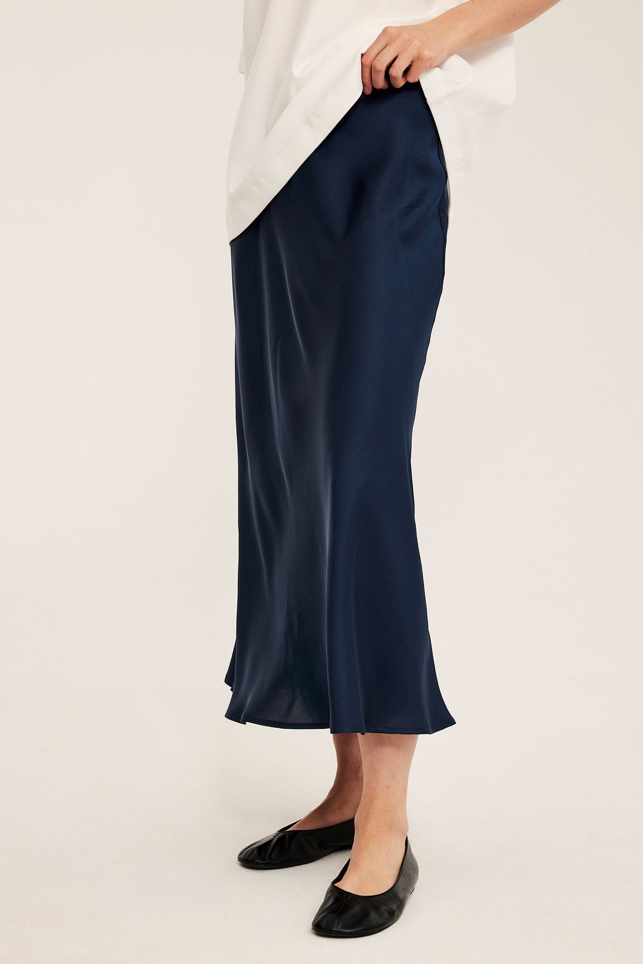 Sivukuva: nainen tummansinisessä kellohelmaisessa satiinihameessa, valkoisessa topissa ja mustissa tasakengissä.