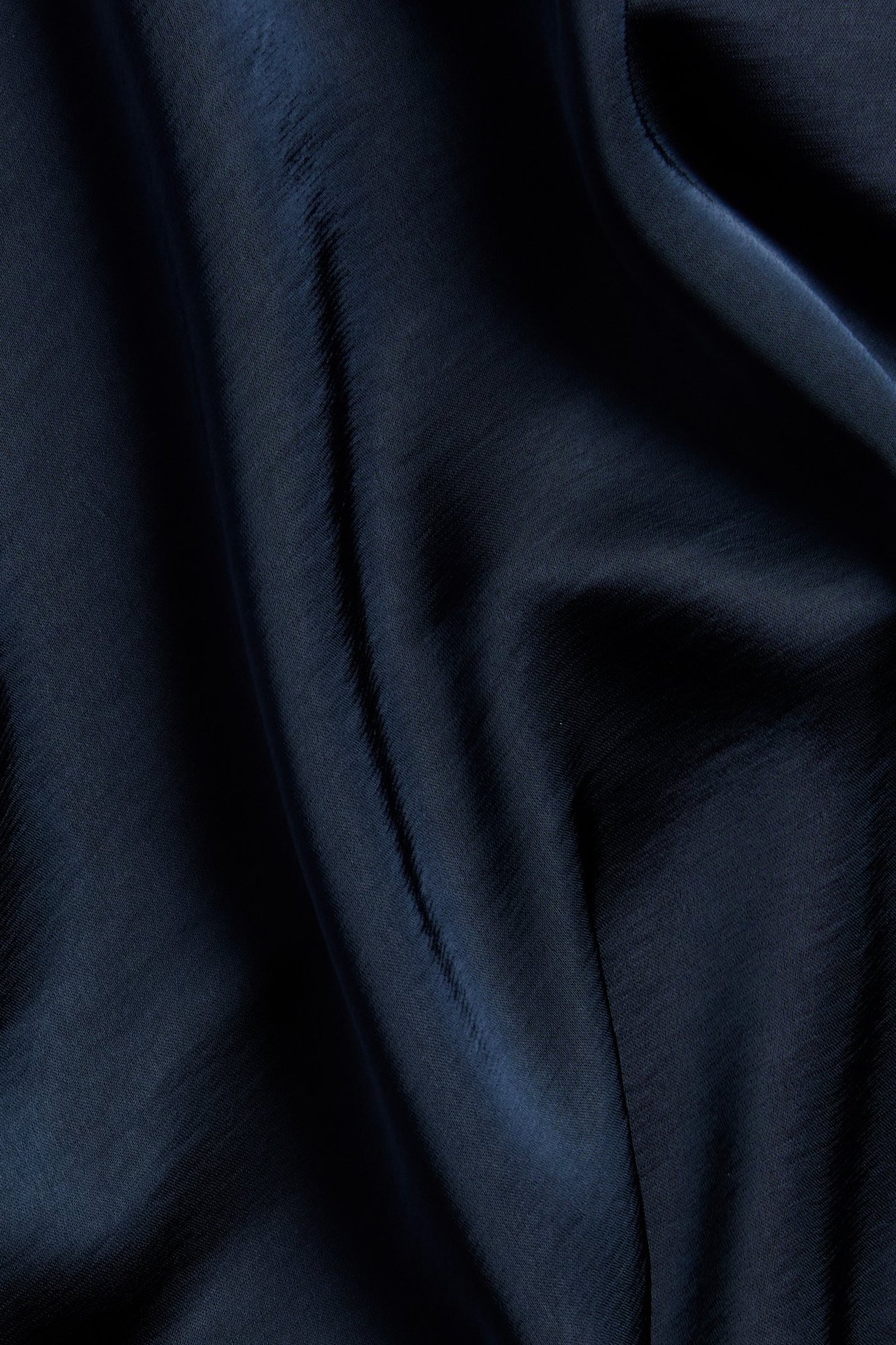 Zbliżenie na ciemnoniebieską, jednolitą tkaninę satynową z poliestru na spódnicę z miękkimi fałdami.