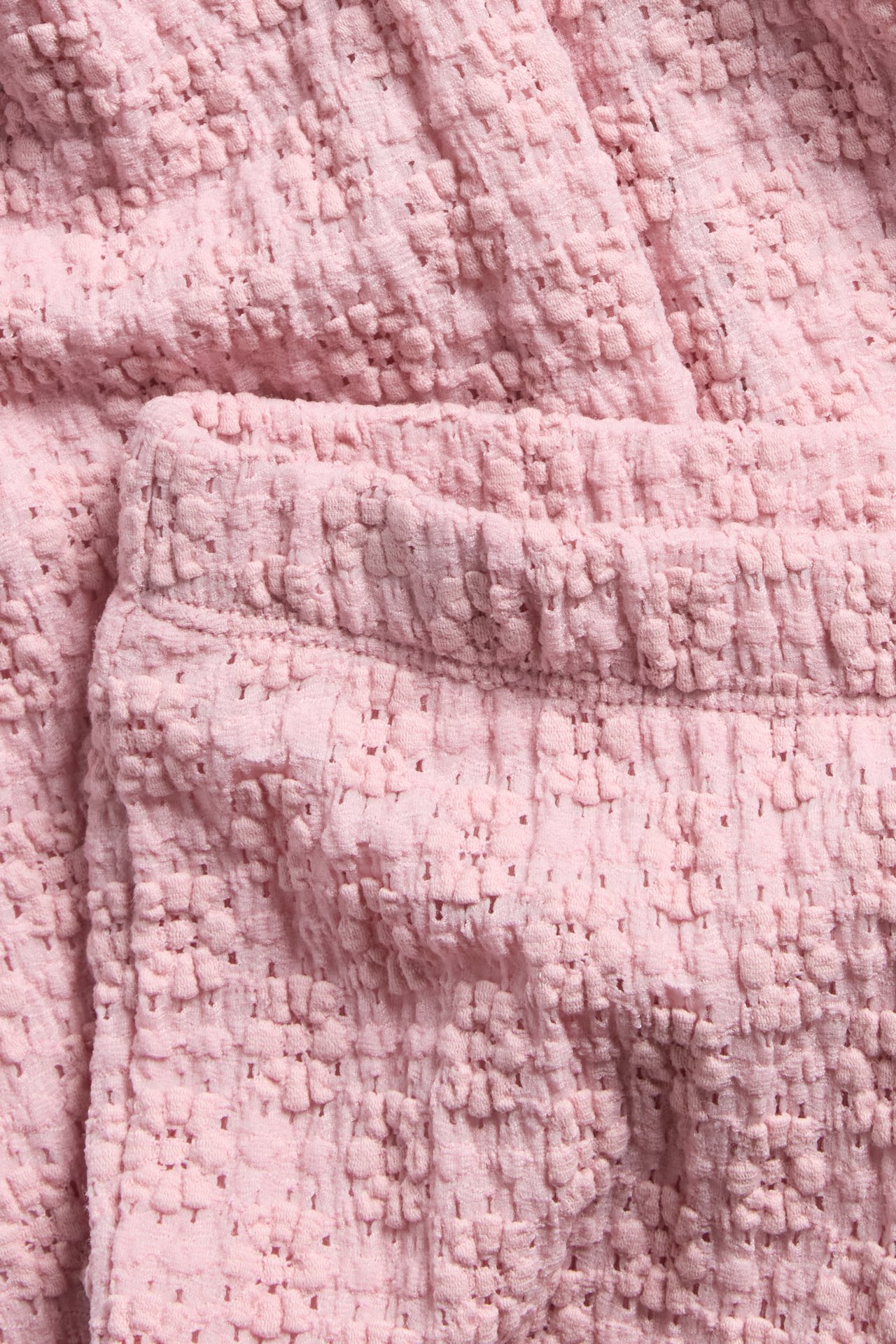 Nærbilde av lyserosa utsvingte blondeleggings med elastisk linning.