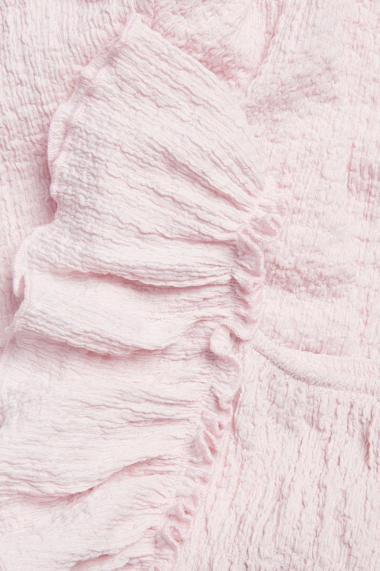 Nærbilde av en lys rosa strukturert jersey jumpsuit med skulder-volanger og smockdetaljer.