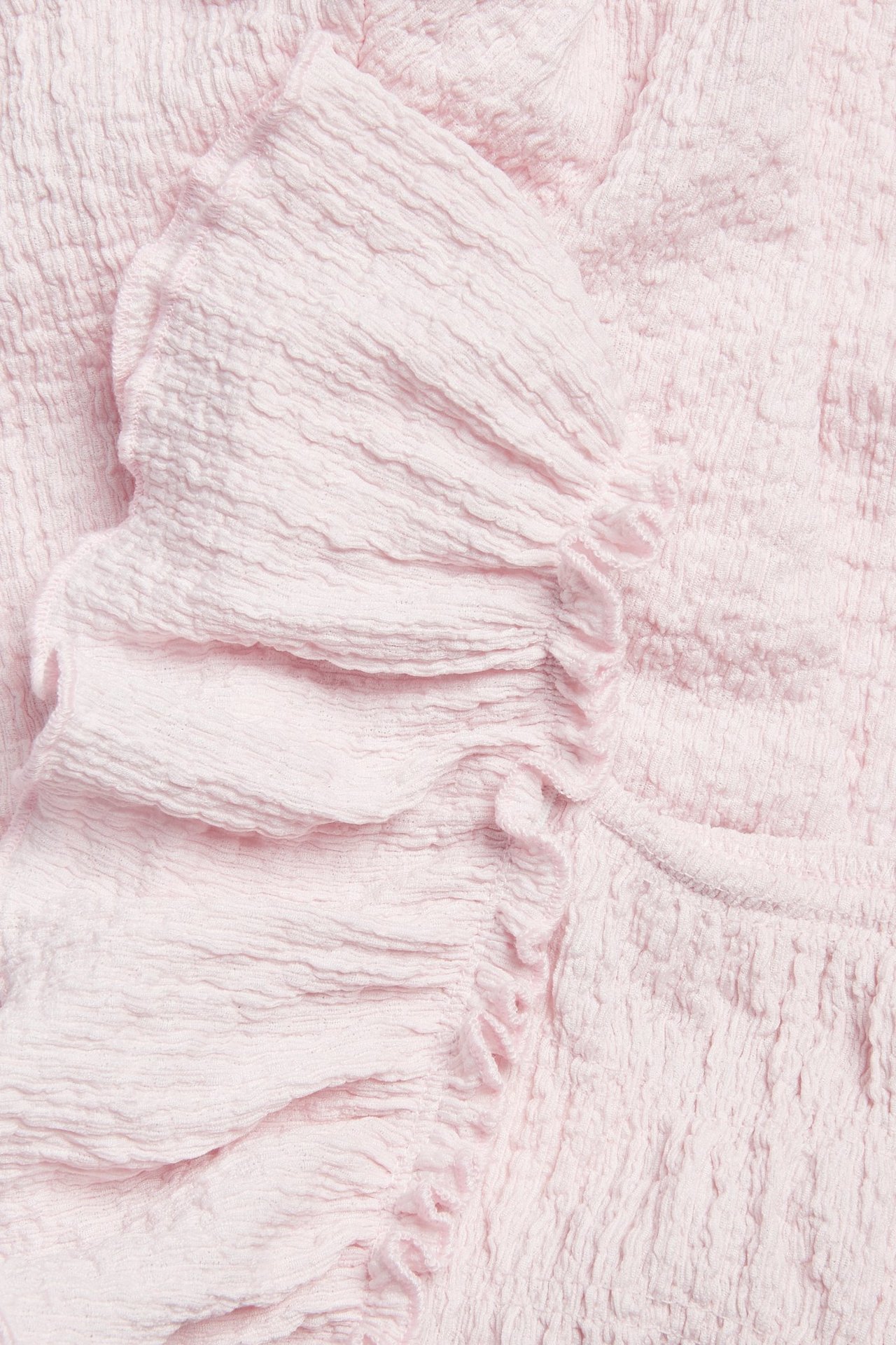 Lähikuva vaaleanpunaisesta rypytetystä trikoohaalarista, jossa on olkarypytyksiä ja smokkireunuksia.