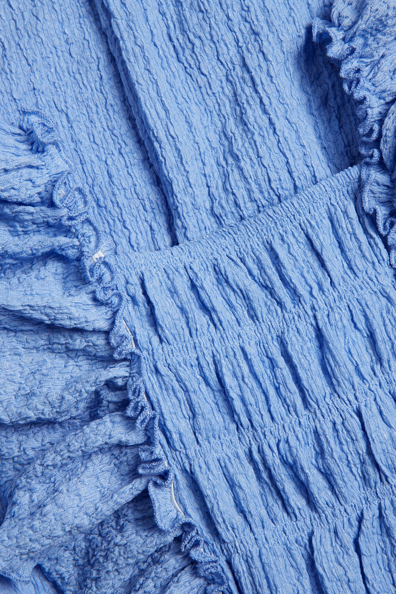 Lähikuva sinisestä tekstuurineulehaalarista, jossa on smokkiryppy ja röyhelö.