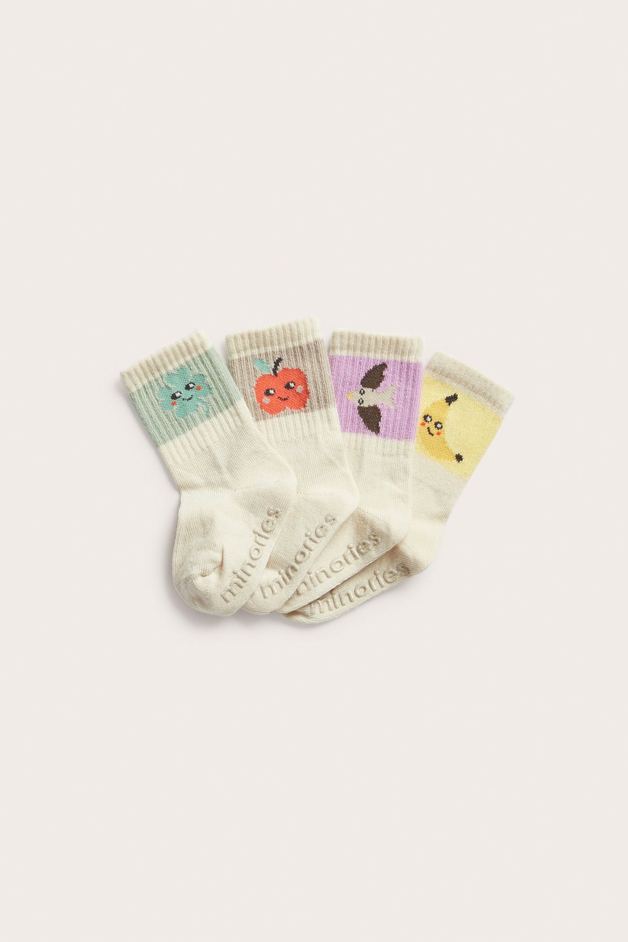 Ovanifrån: Fyra par beiga babystrumpor med färgglada frukt- och grönsaksmönster, inklusive halkskyddsloggor.