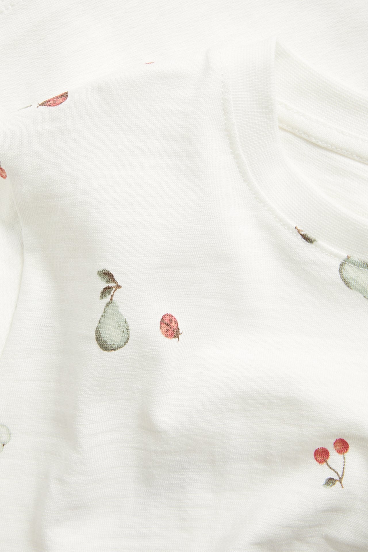 Zbliżenie: T-shirt z bawełny slub w kolorze off-white z wzorem gruszek, wiśni i biedronek.