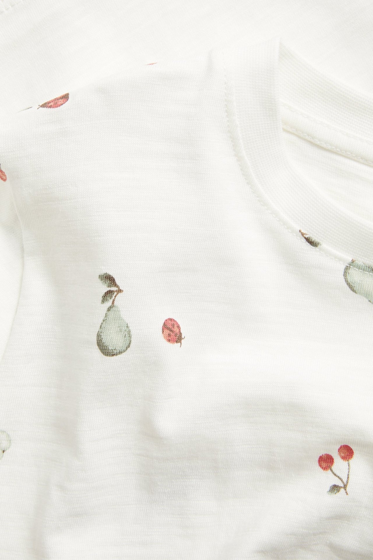 Nærbilde: Offwhite slub bomull t-skjorte med mønster av pærer, kirsebær og marihøner.