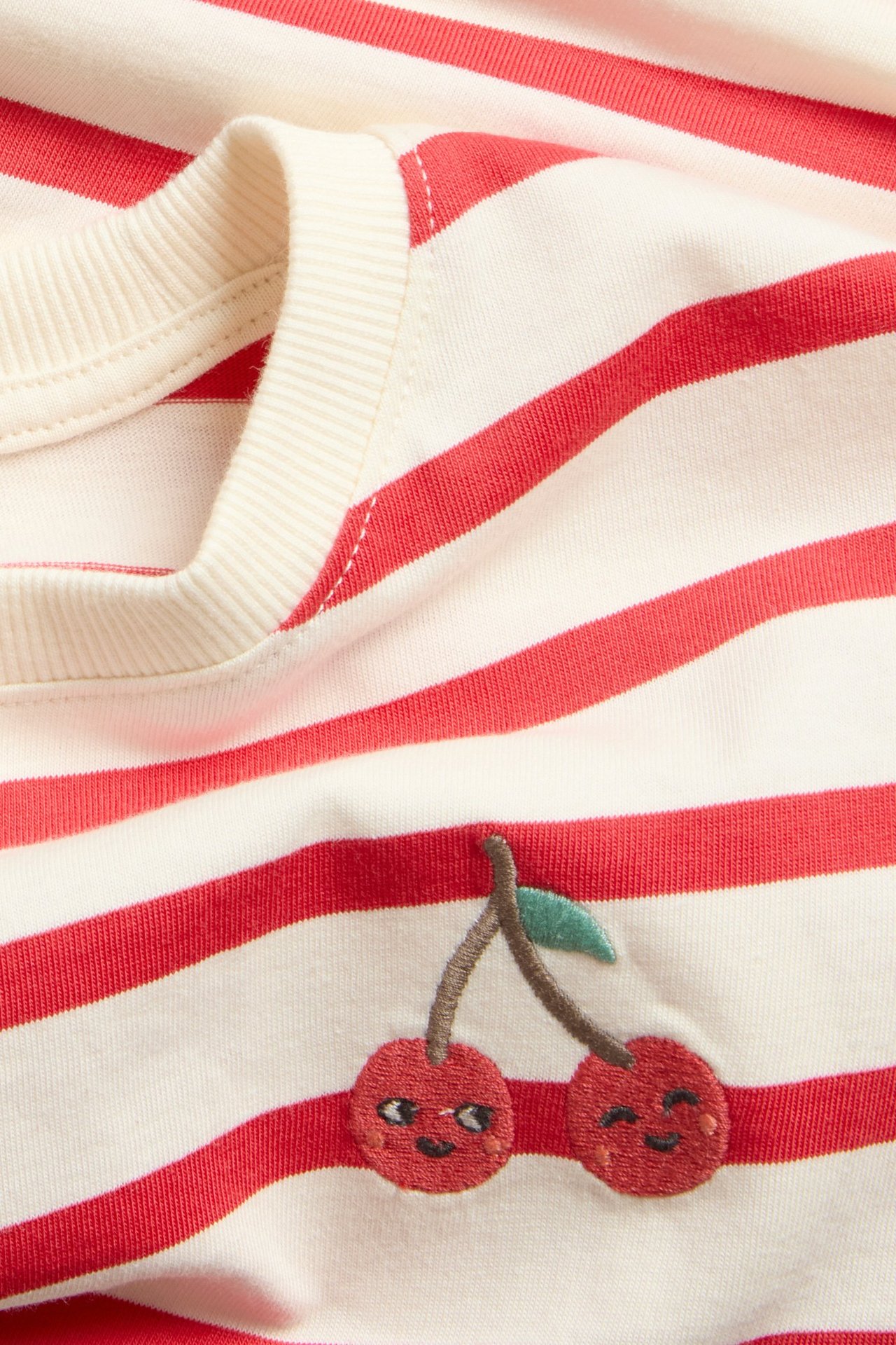 Närbild på en randig kortärmad t-shirt i bomull med röda och benvita ränder samt körsbärsbrodyr.