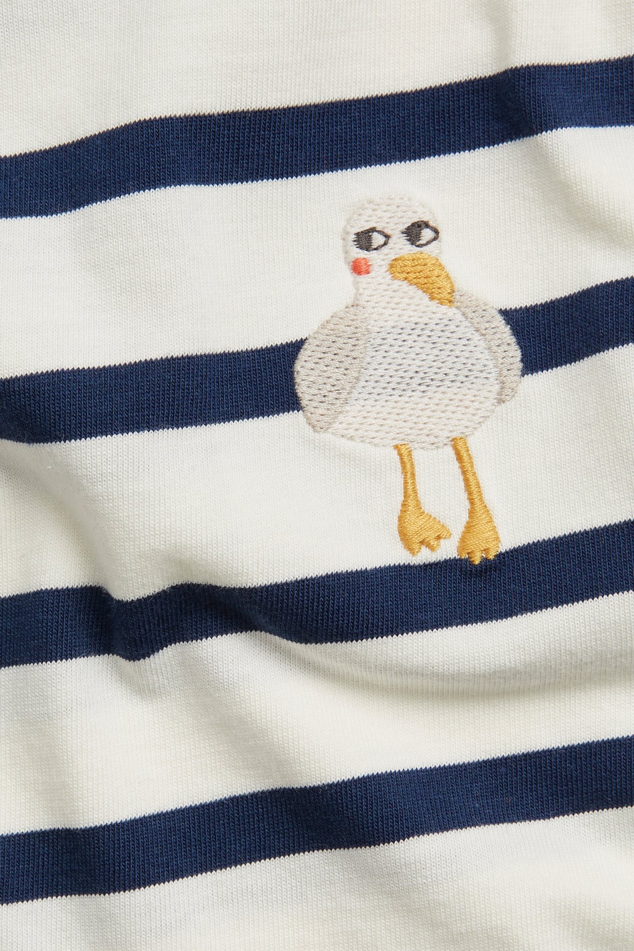 Zbliżenie na biało-granatowy bawełniany T-shirt w paski z haftowaną mewą.