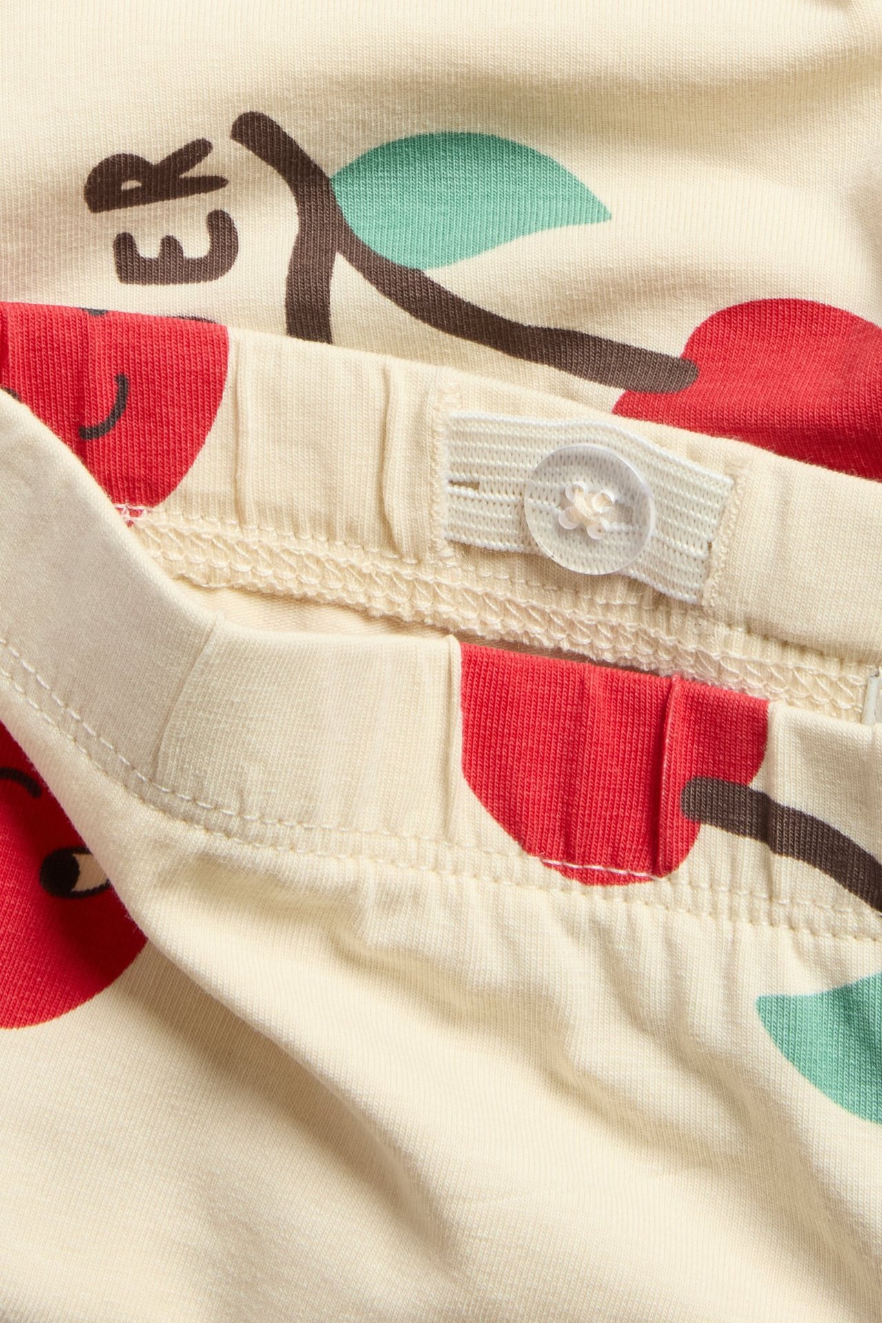 Lähikuva: beiget lasten pyöräilyhousut kirsikkakuviolla ja säädettävällä joustovyötäröllä.