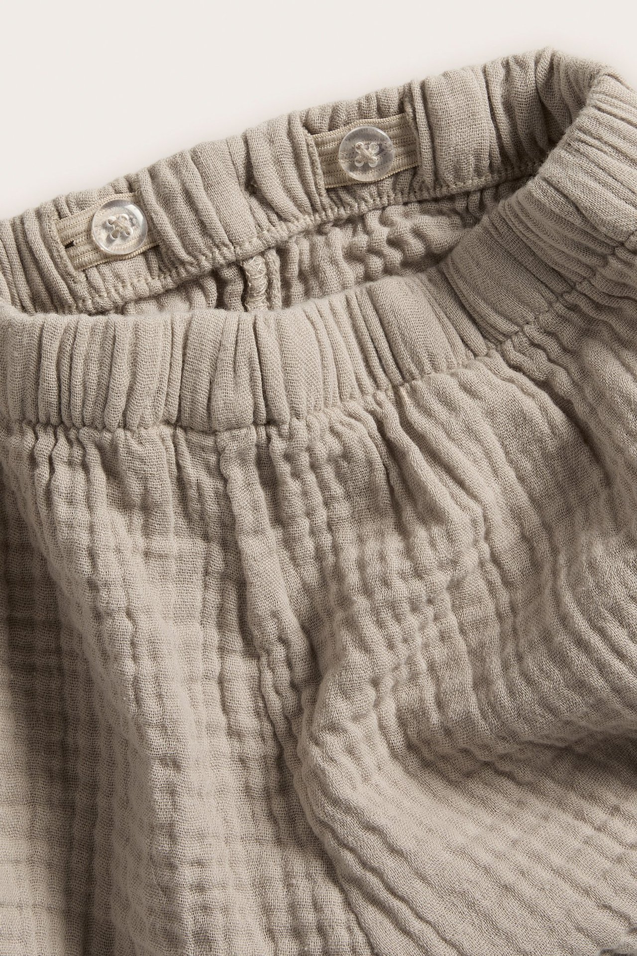 Nærbilde av beige vevde babyshorts med elastisk midje og dekorative gjennomsiktige knapper.